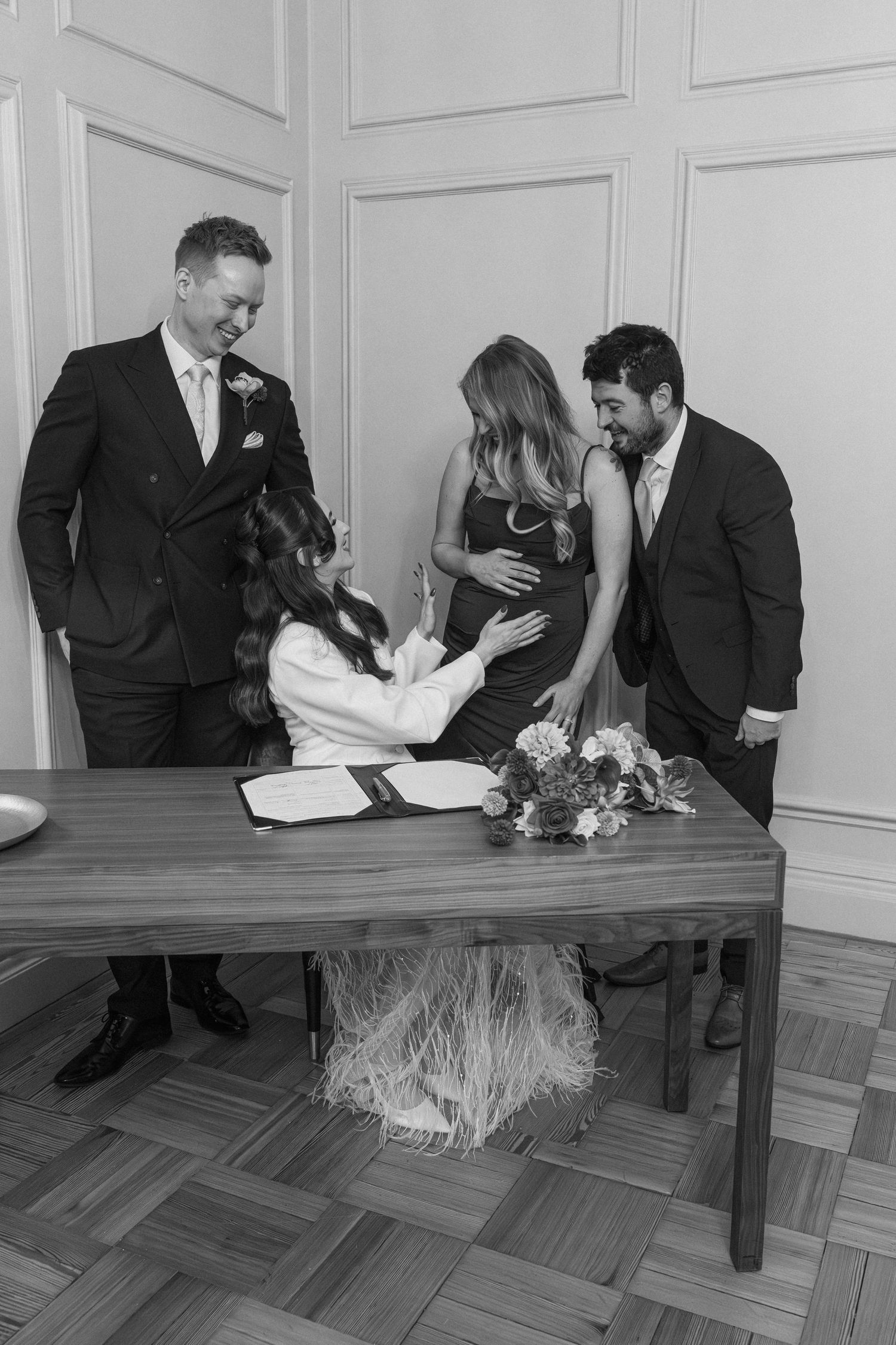 Black and white photo of bride signing wedding register with witnesses at registry office.
