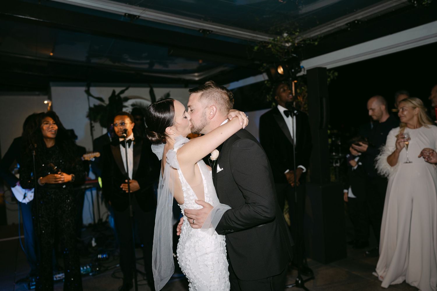 A bride in a white lace gown dances with her partner at an indoor wedding reception.