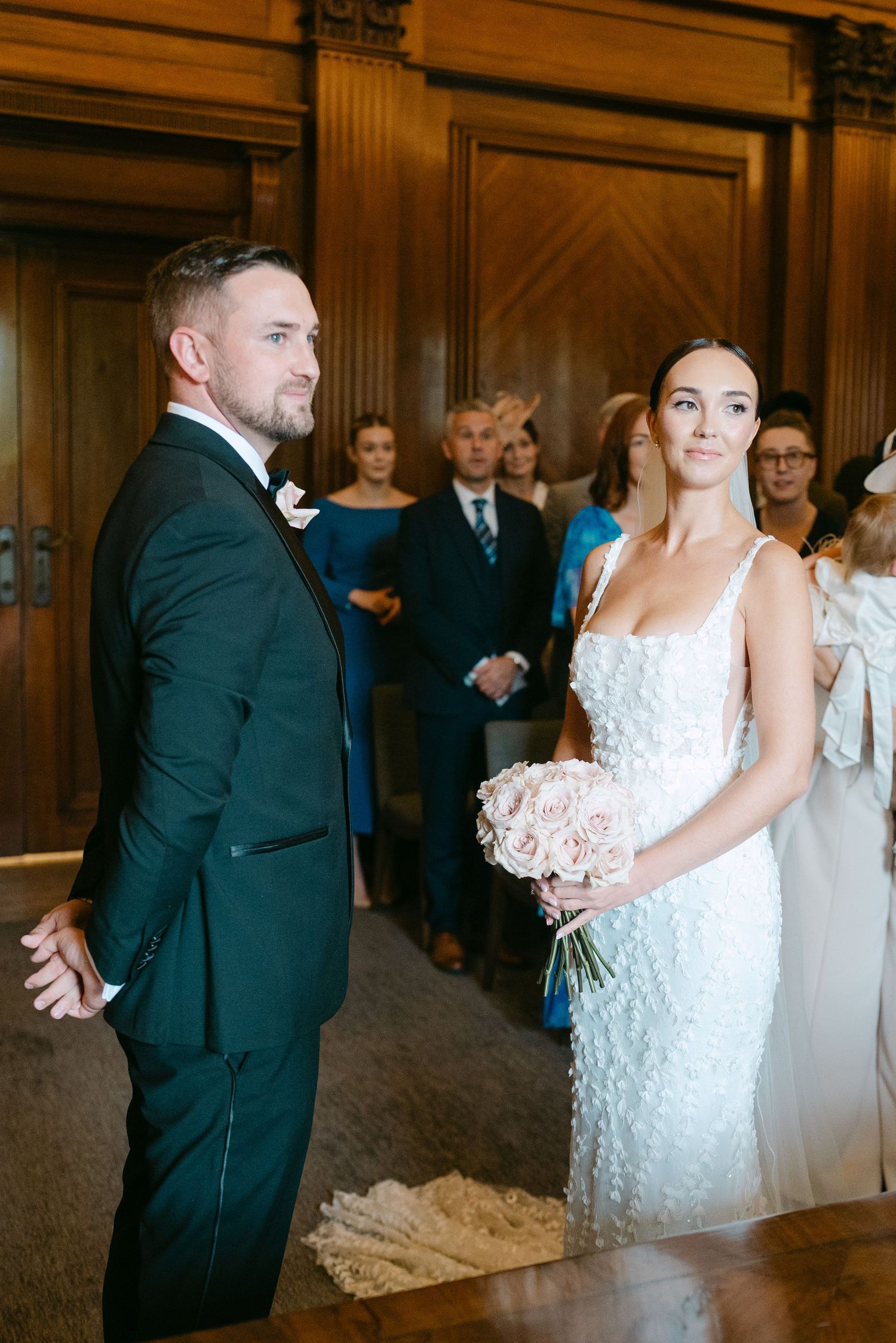 Wedding party members pose in an elegant wood-paneled hallway during celebration.