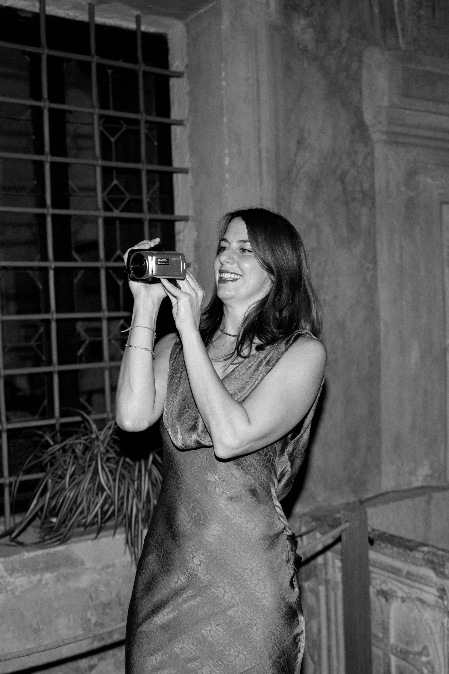 Person in sparkly dress laughing and dancing in front of large windows at night.