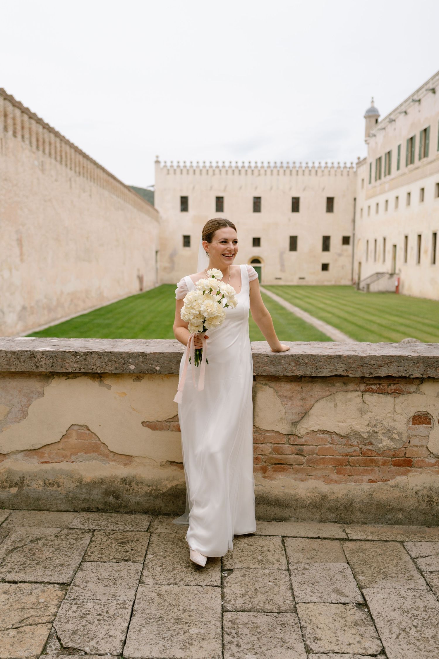 Wedding photo at historic castle venue with manicured lawn and cream colored walls.