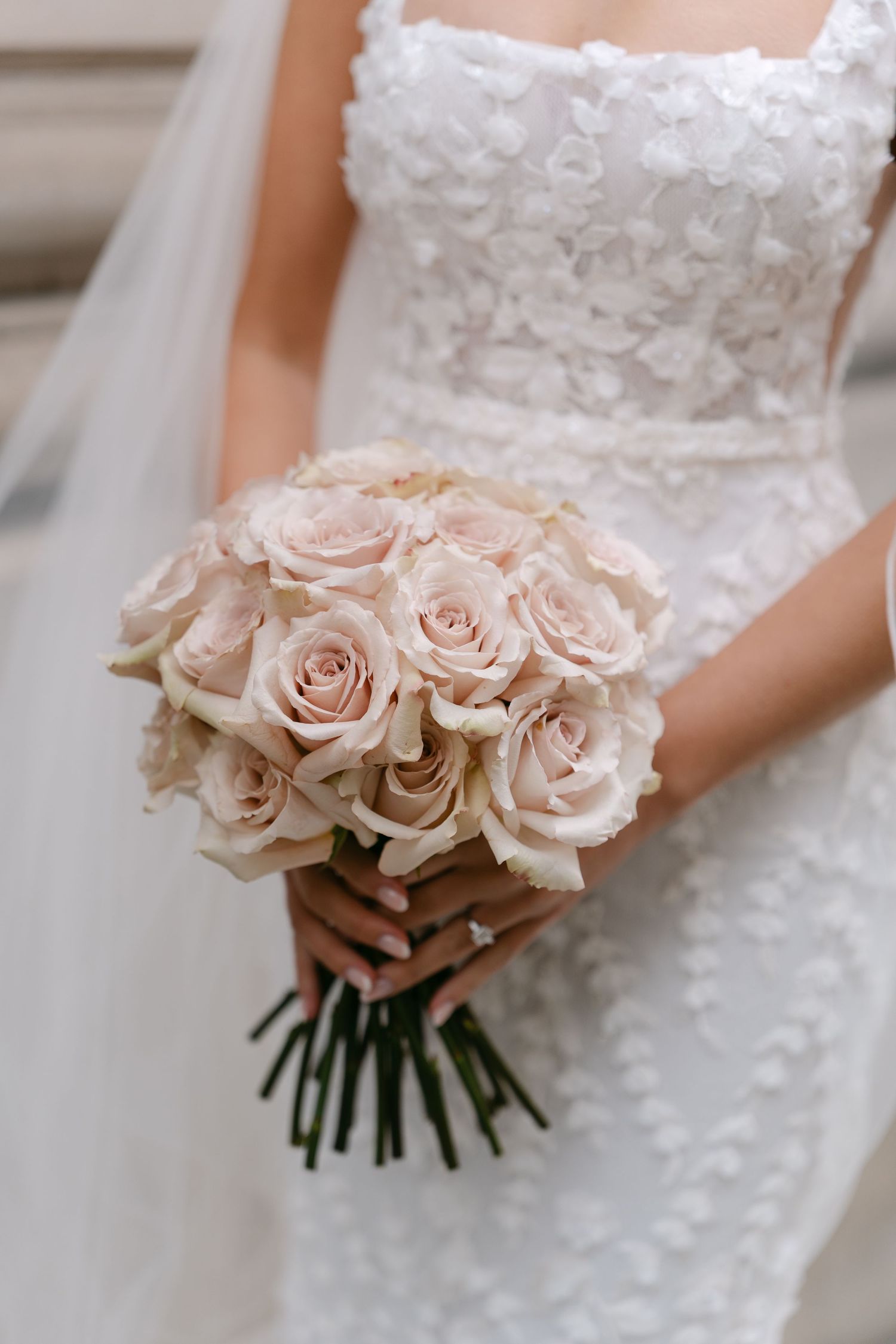 Close-up of bridal bouquet featuring blush pink roses against white lace wedding dress.
