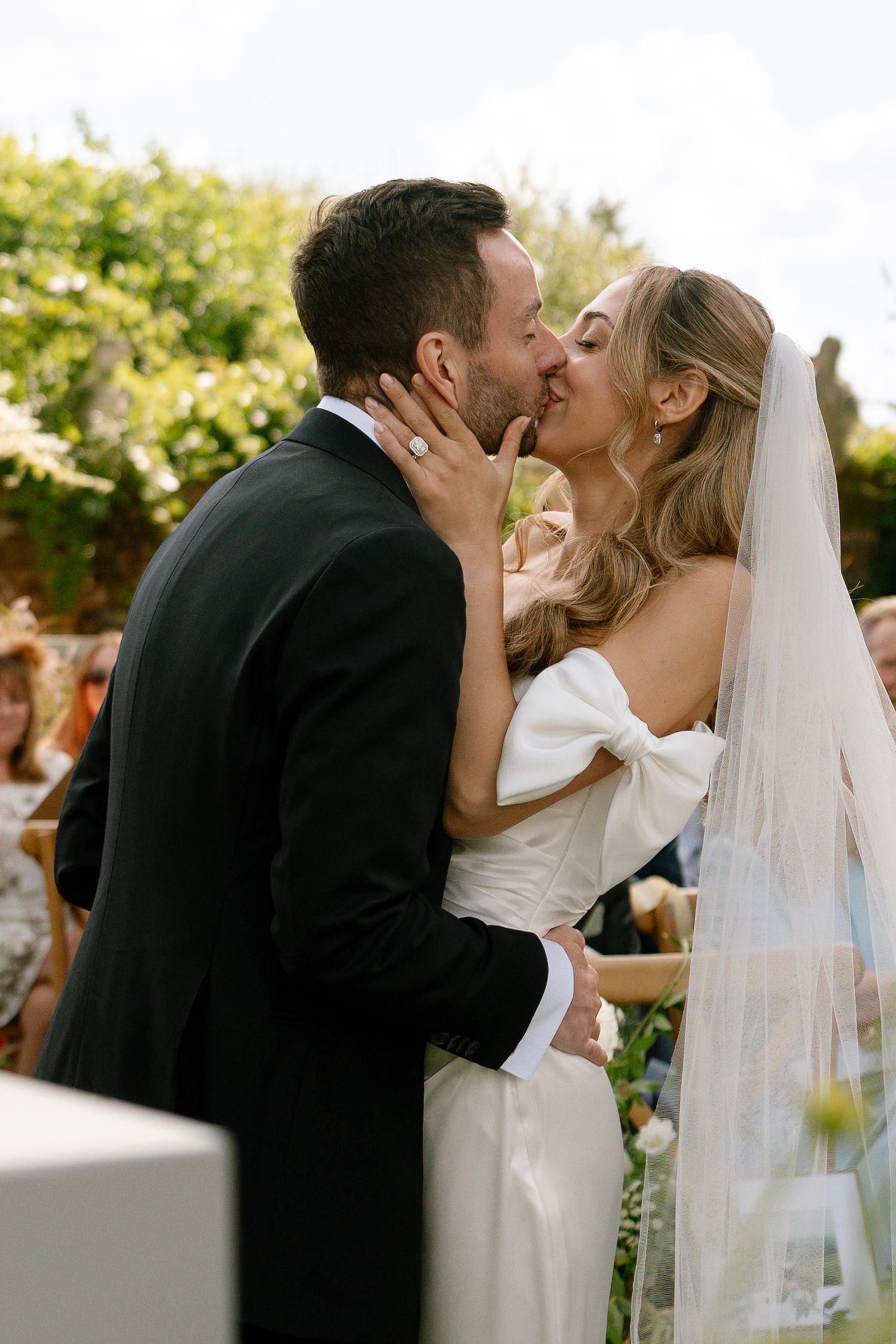 Newlyweds share their first kiss during an outdoor garden wedding ceremony.