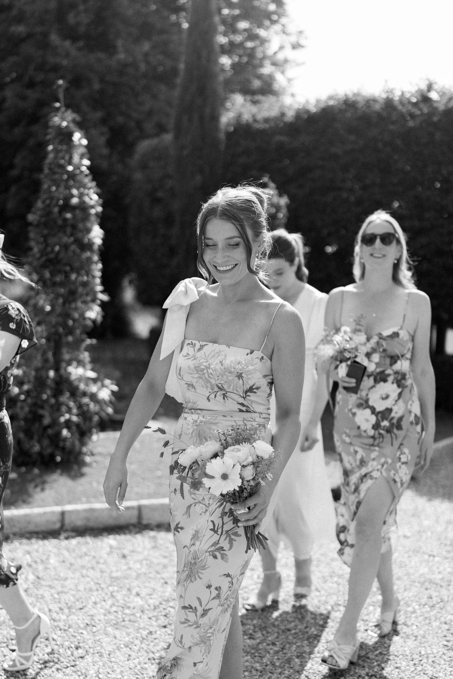 Bridesmaids in floral dresses walking outdoors holding bouquets.