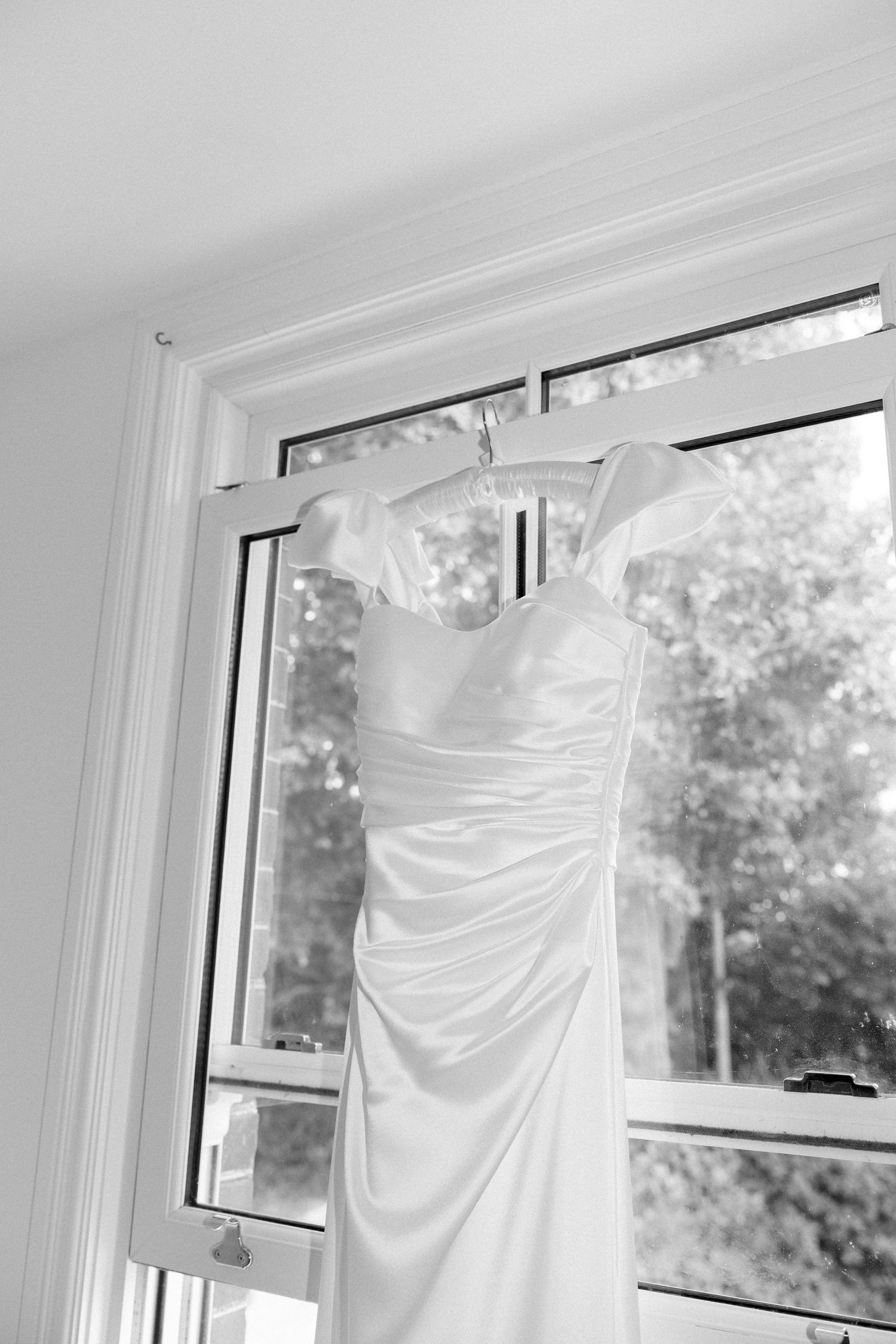 White wedding dress hanging by window with natural light streaming through.