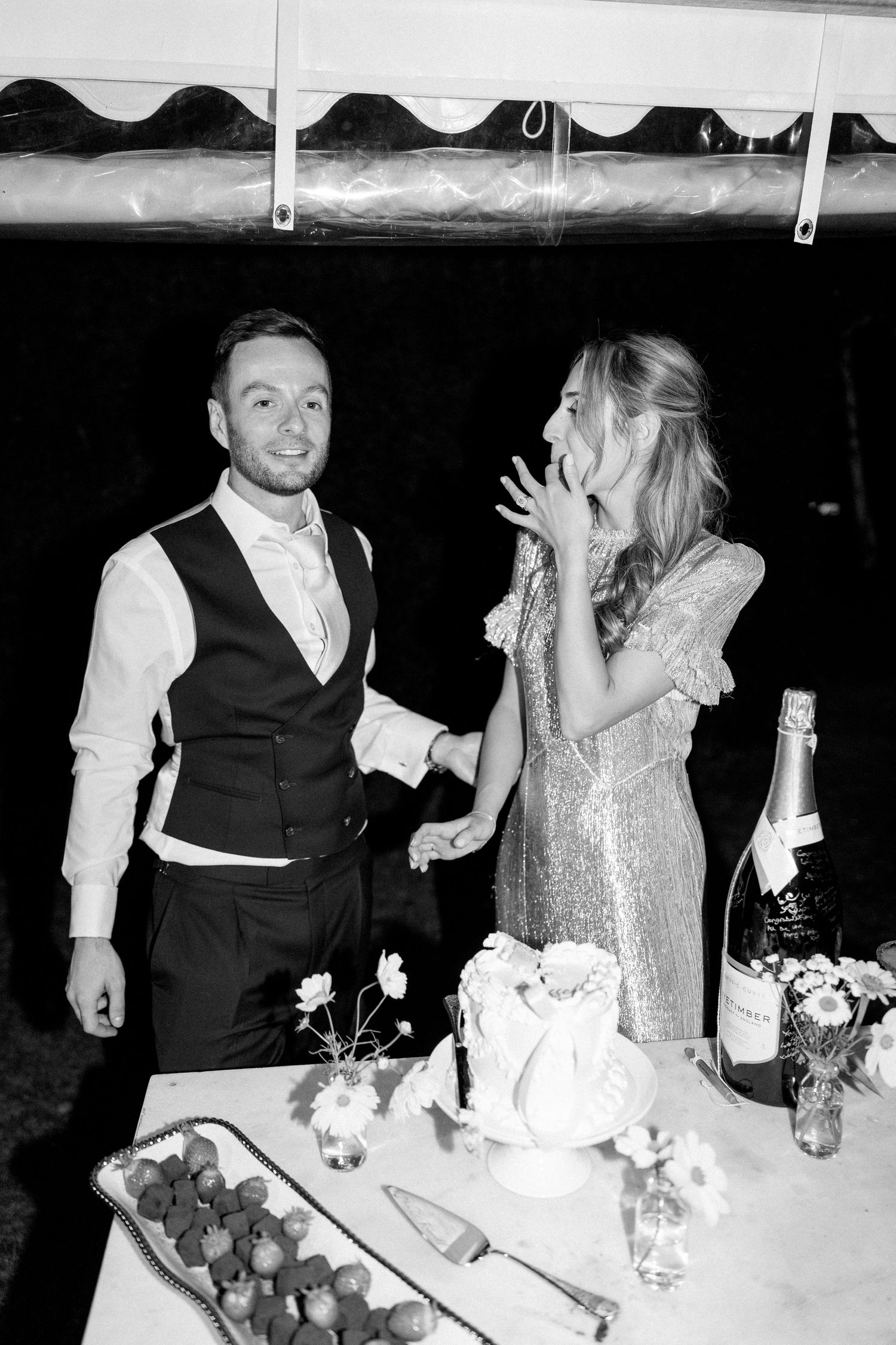 A couple shares laughter while cutting cake at their wedding reception.