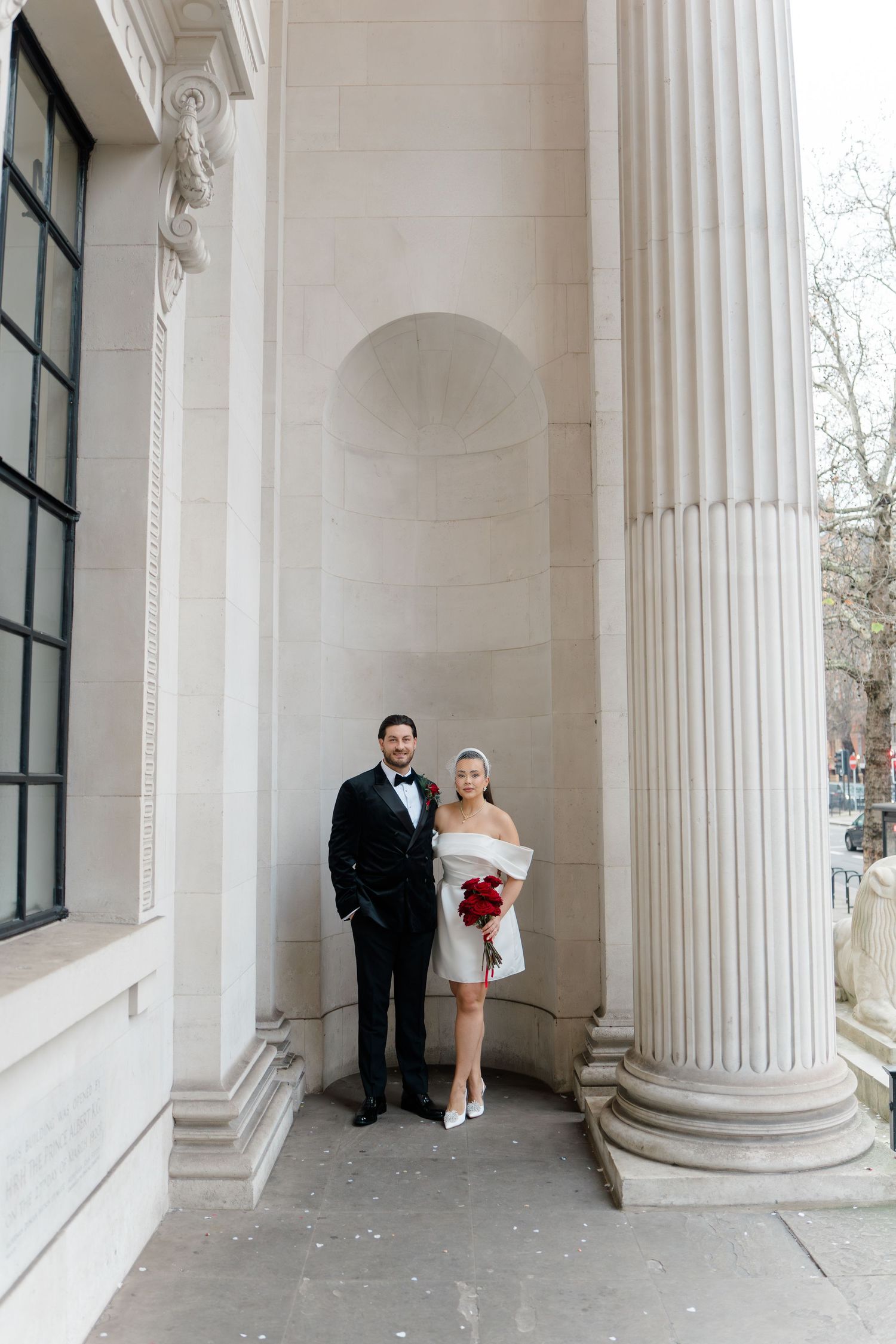 Wedding couple poses between classical white columns in architectural photo series.