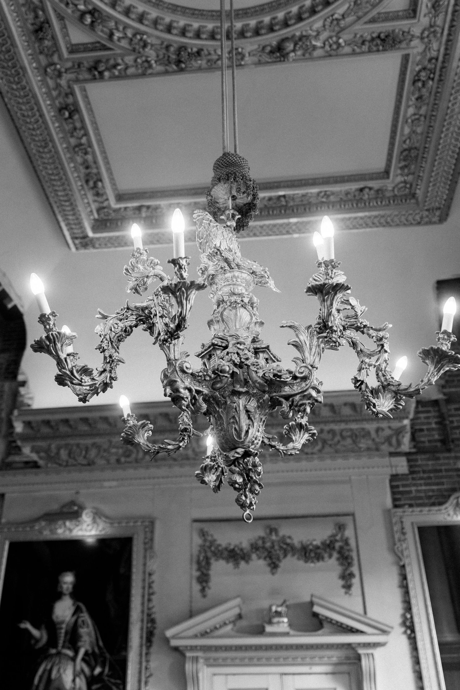 Ornate Rococo chandelier with candle lights hanging from decorative plasterwork ceiling in elegant historic room.