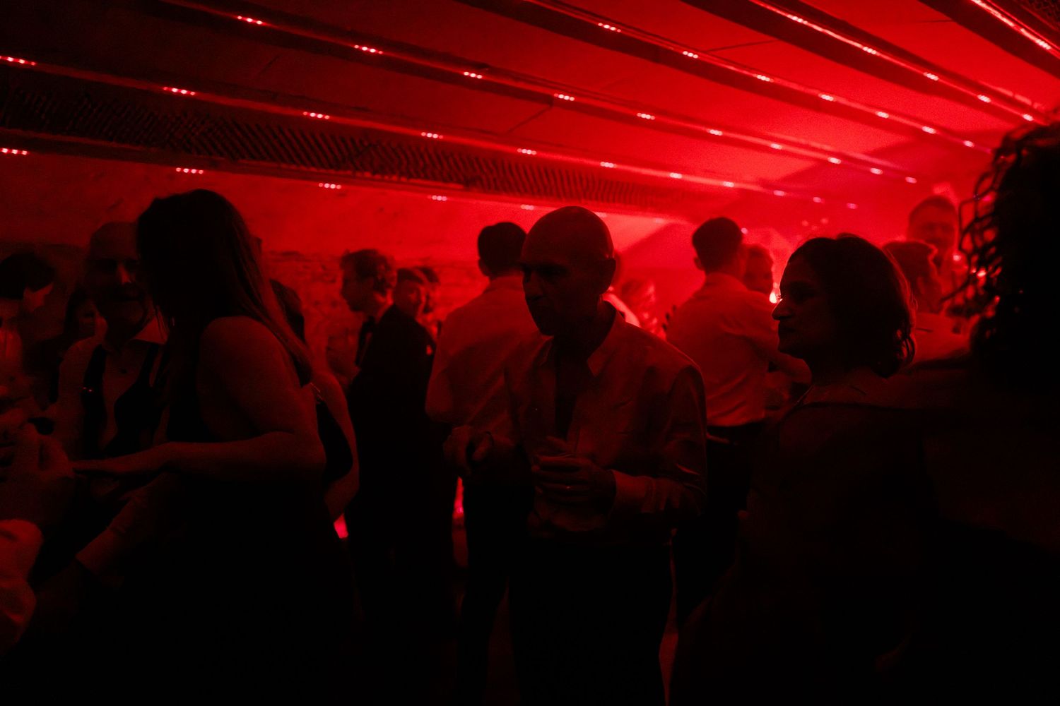 People socializing at a nightclub party under dramatic red lighting creating a moody atmospheric scene.