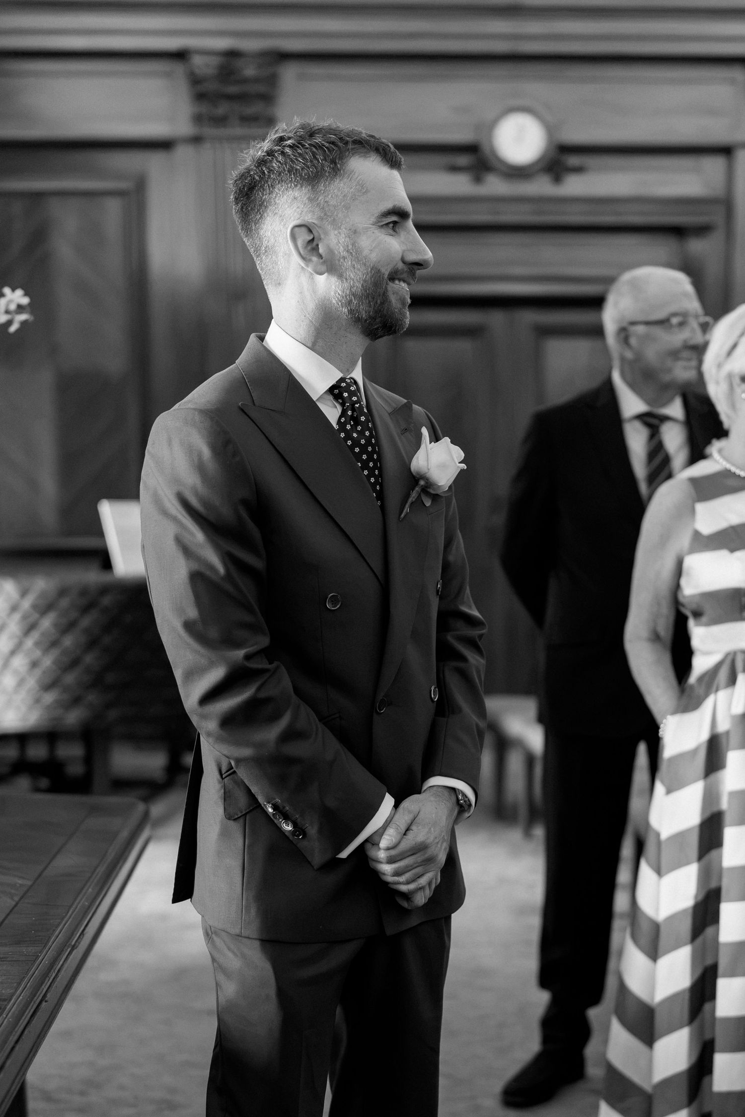 Black and white portrait of groom in dark suit with boutonniere smiling at wedding ceremony altar.