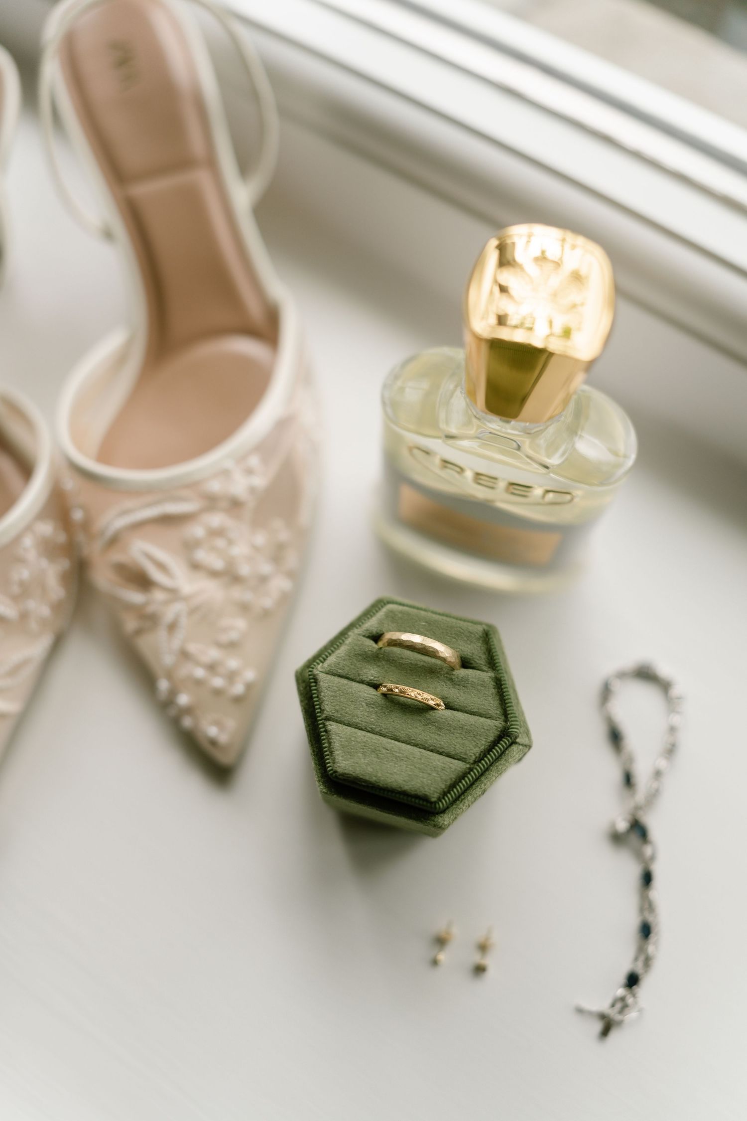 Elegant blush wedding shoes arranged with a green velvet ring box in natural window light.