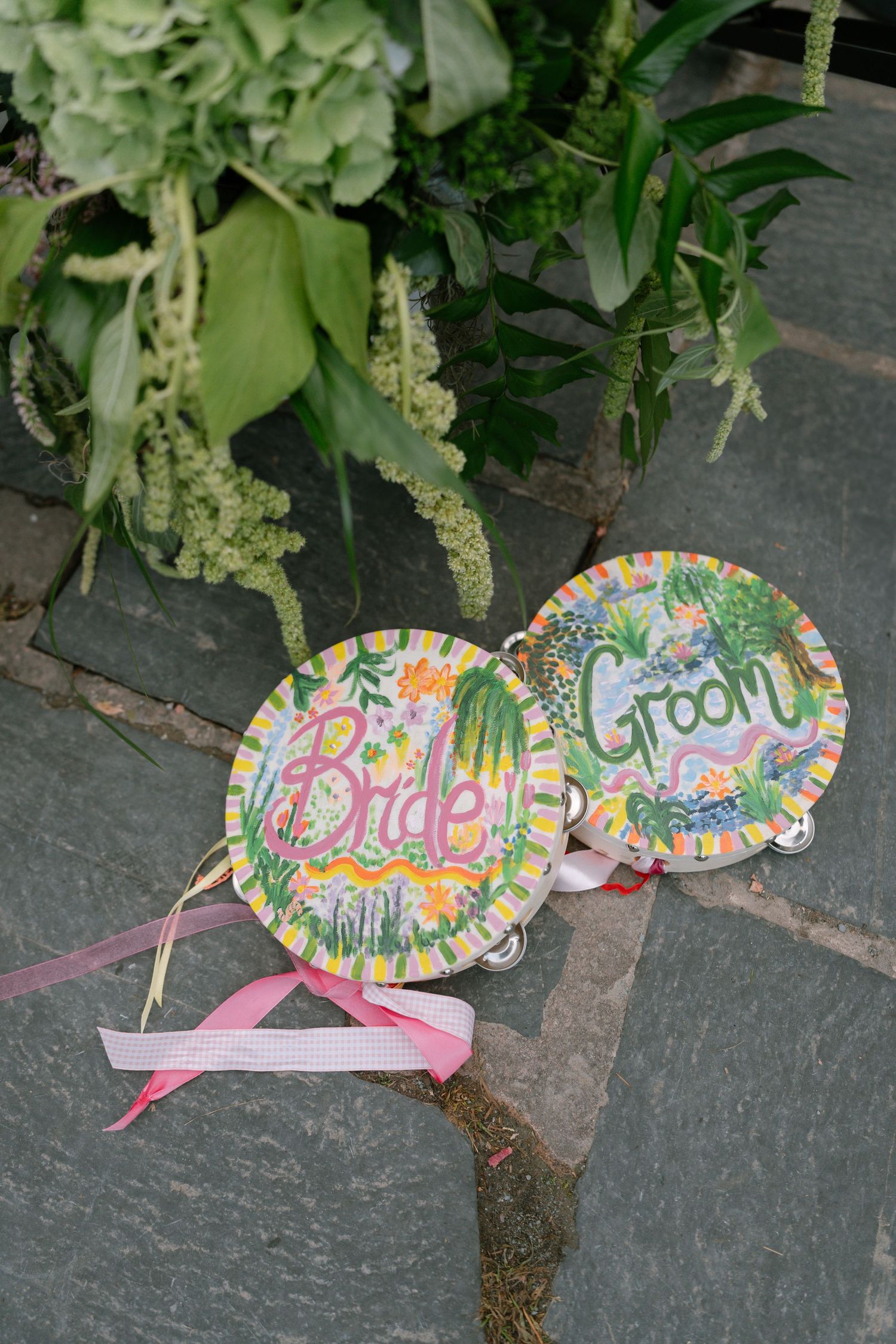 Colorful handmade bride and groom signs with floral designs against greenery.