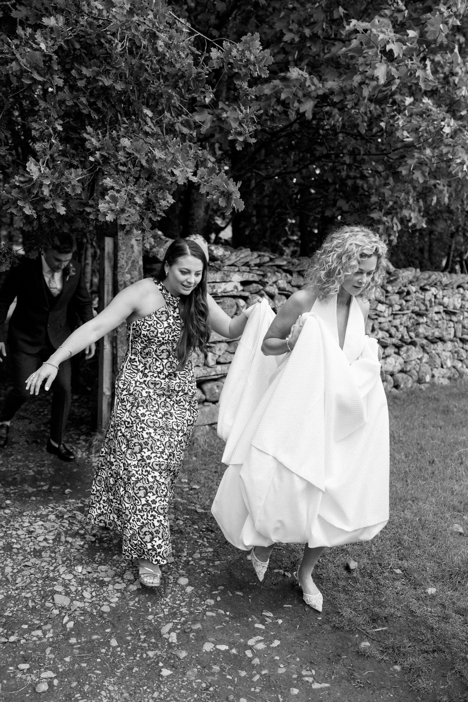 Playful black and white photos of wedding guests dancing on grass.