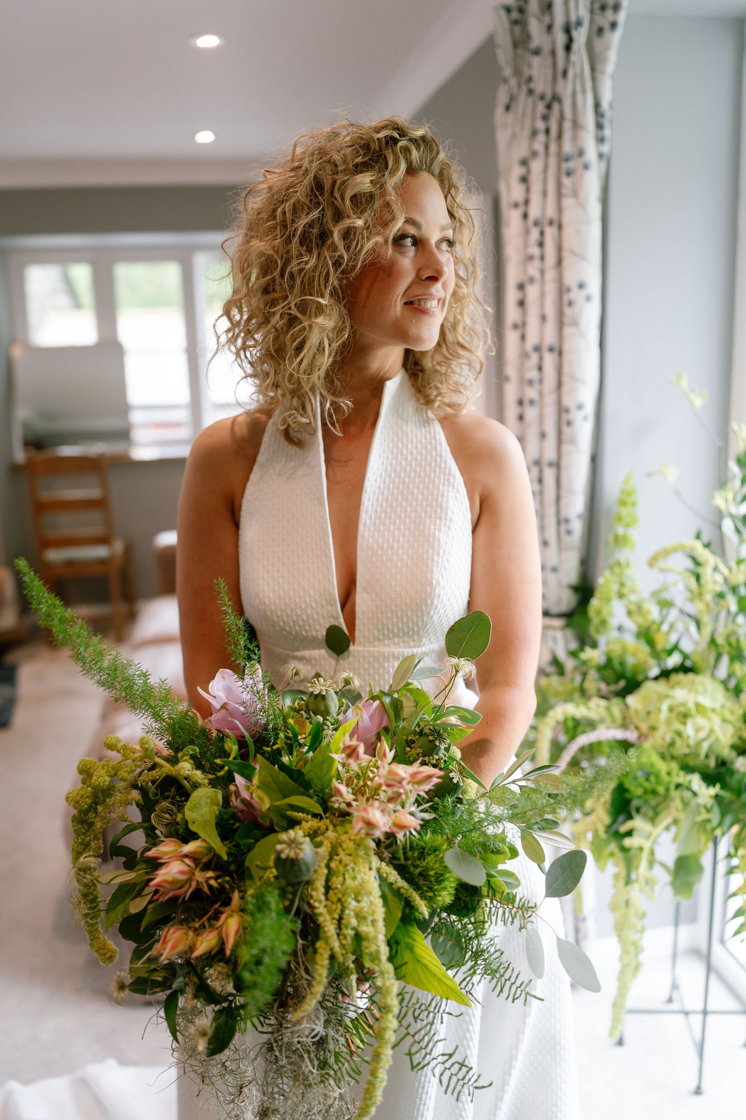 A wedding portrait featuring a halter neck white dress and vibrant natural bouquet with greenery and pink flowers.