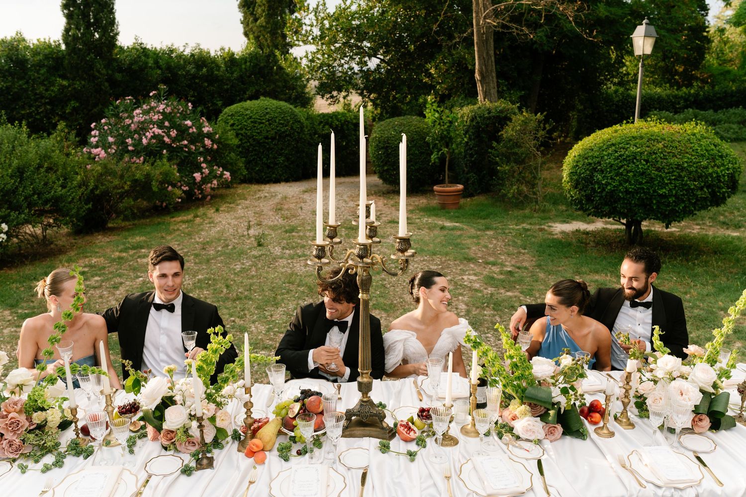 An elegant outdoor wedding reception table decorated with floral arrangements and candles at sunset.