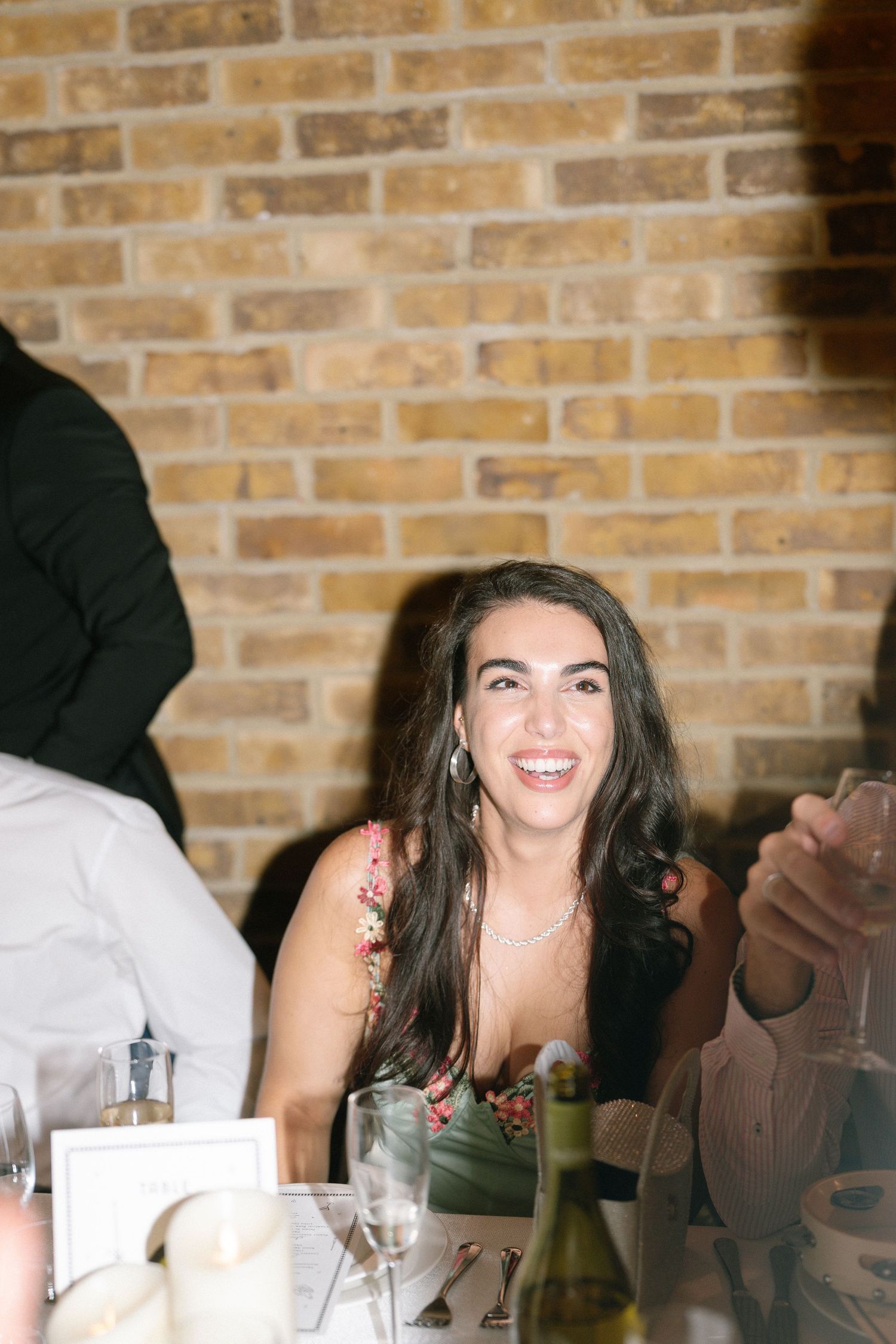 A candid moment at a wedding reception with guests laughing at a brick-walled venue.
