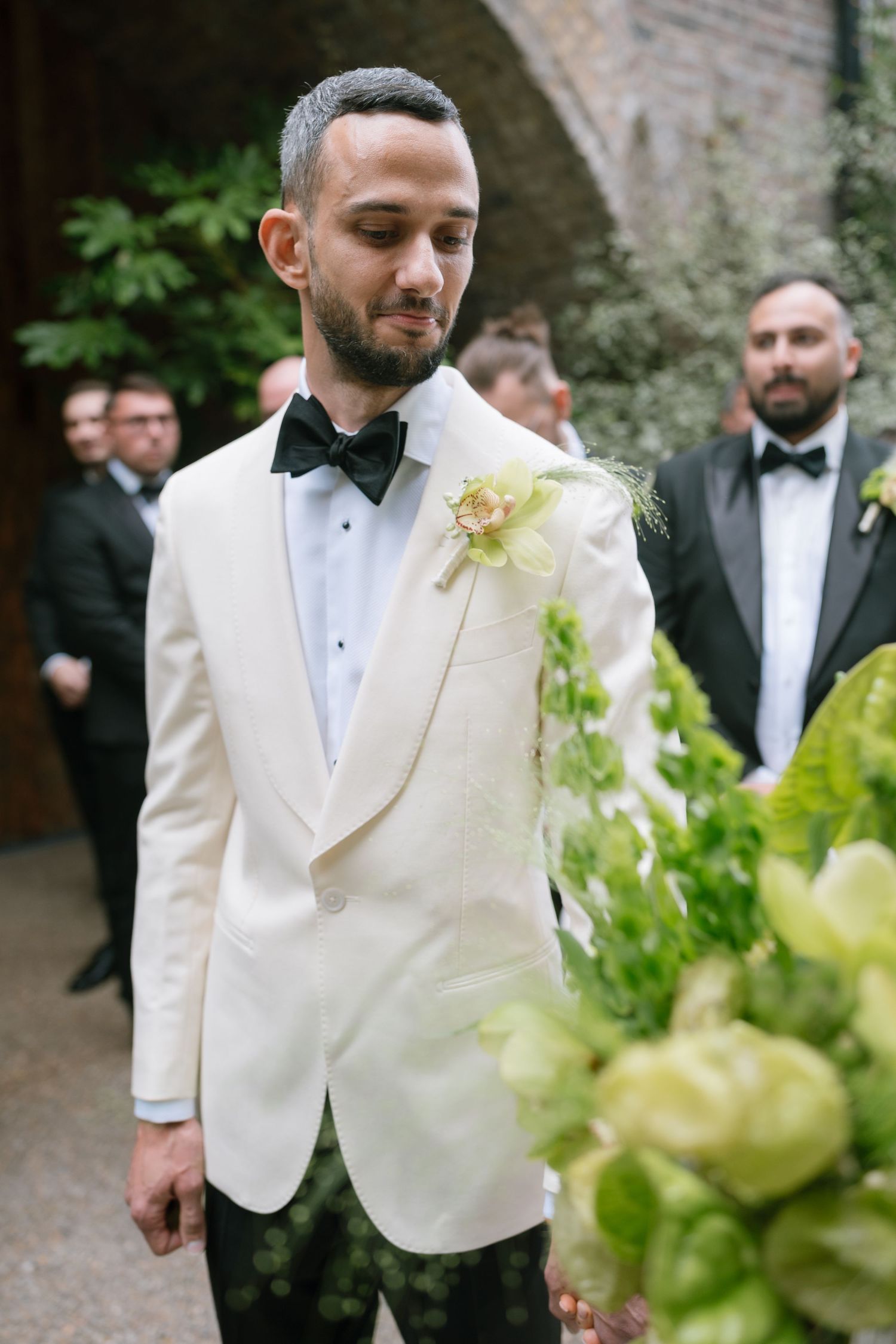Wedding party members in formal attire gather in an outdoor garden setting.