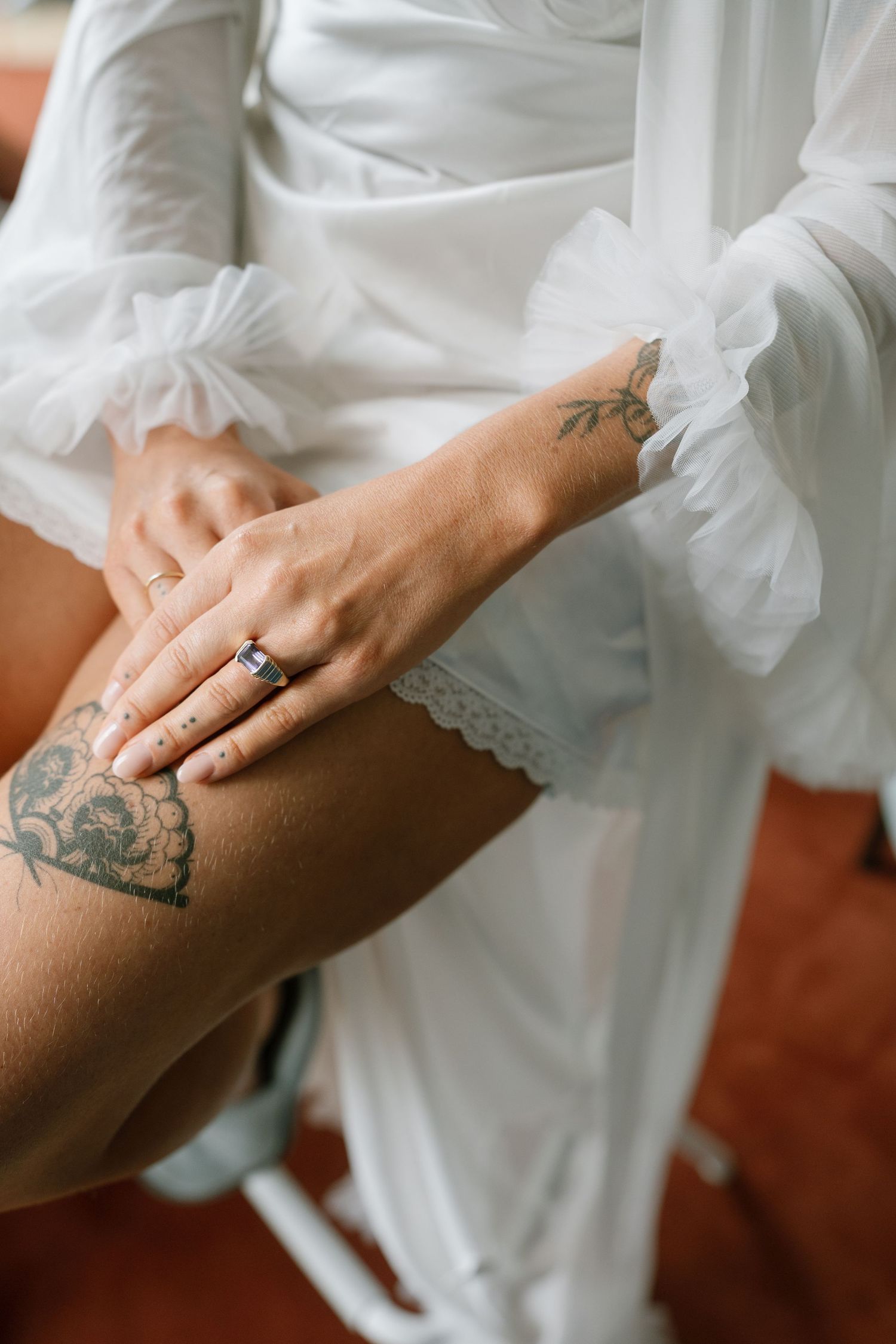 Close-up of a tattooed hand wearing an engagement ring with white lace dress fabric.