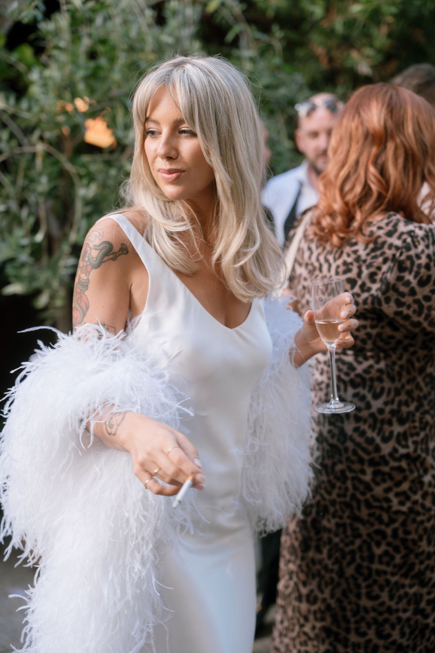 Bride in a white feathered dress mingles with guests at an outdoor wedding reception.