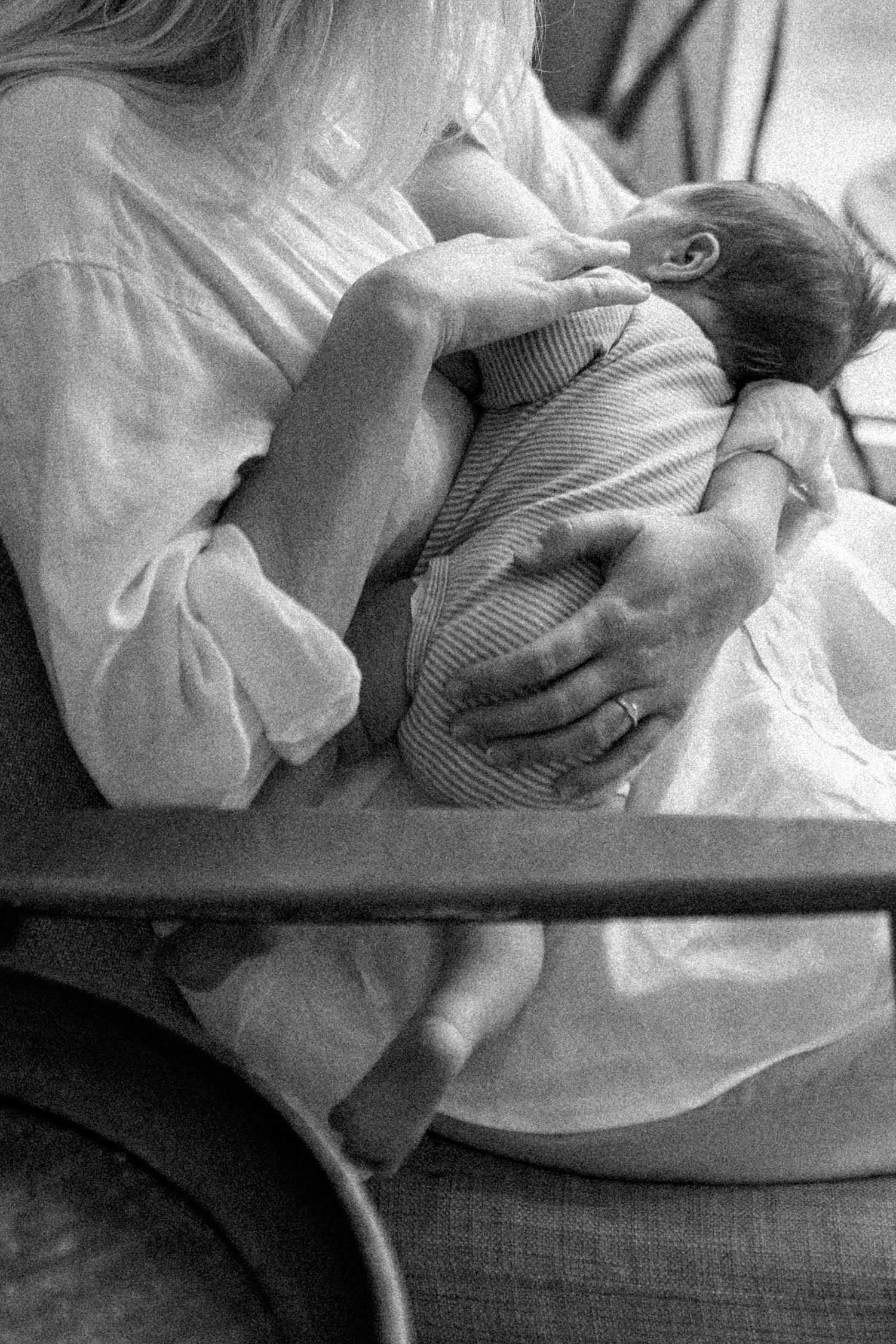 A tender black and white photograph of a newborn baby being cradled and fed in soft natural light.
