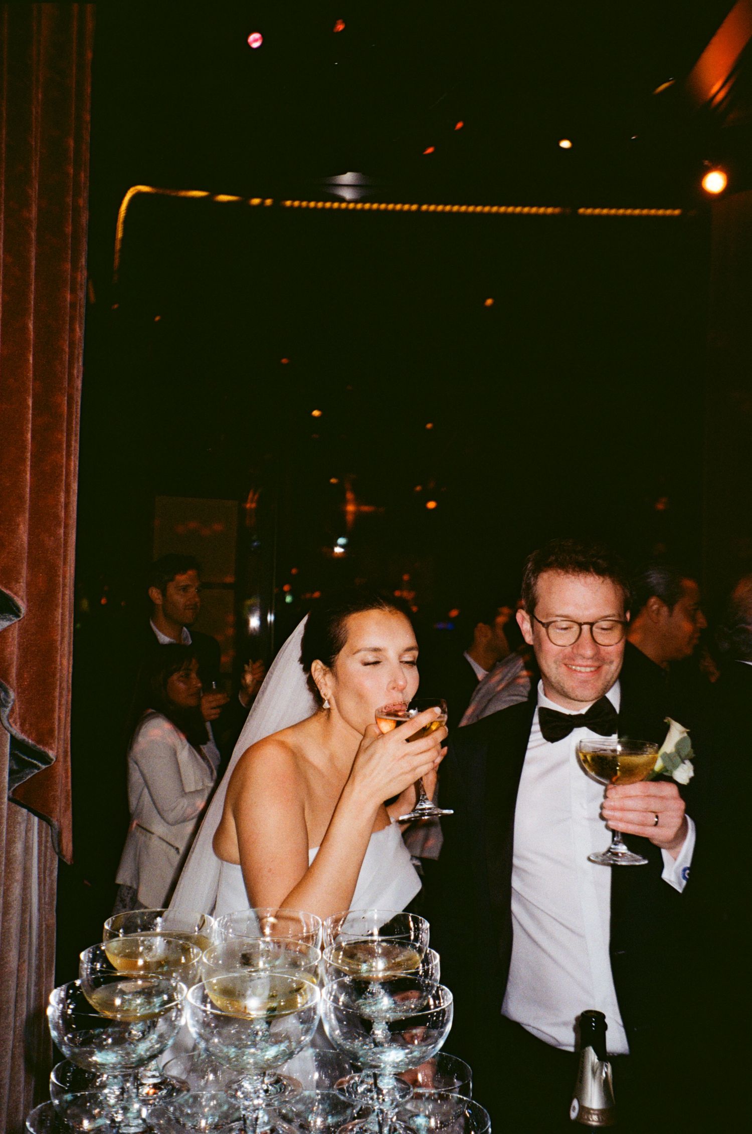 Wedding guests laugh and drink together at a formal reception with champagne glasses on the table.