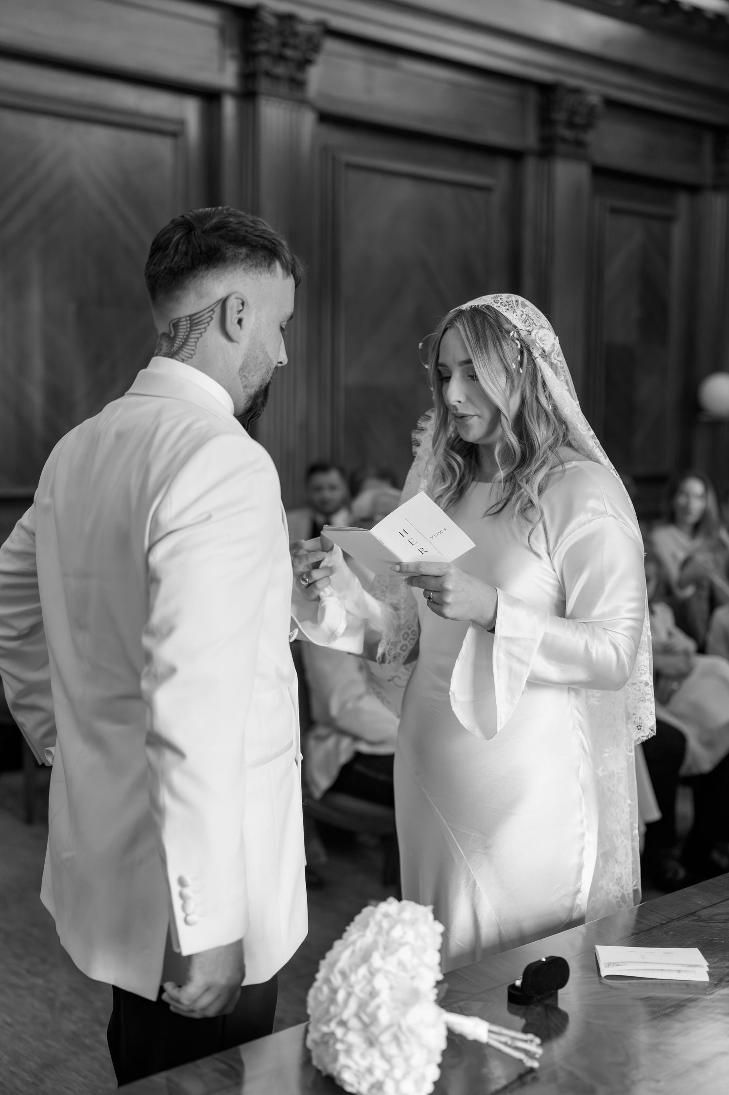 Black and white wedding ceremony photo showing couple exchanging vows in formal attire.