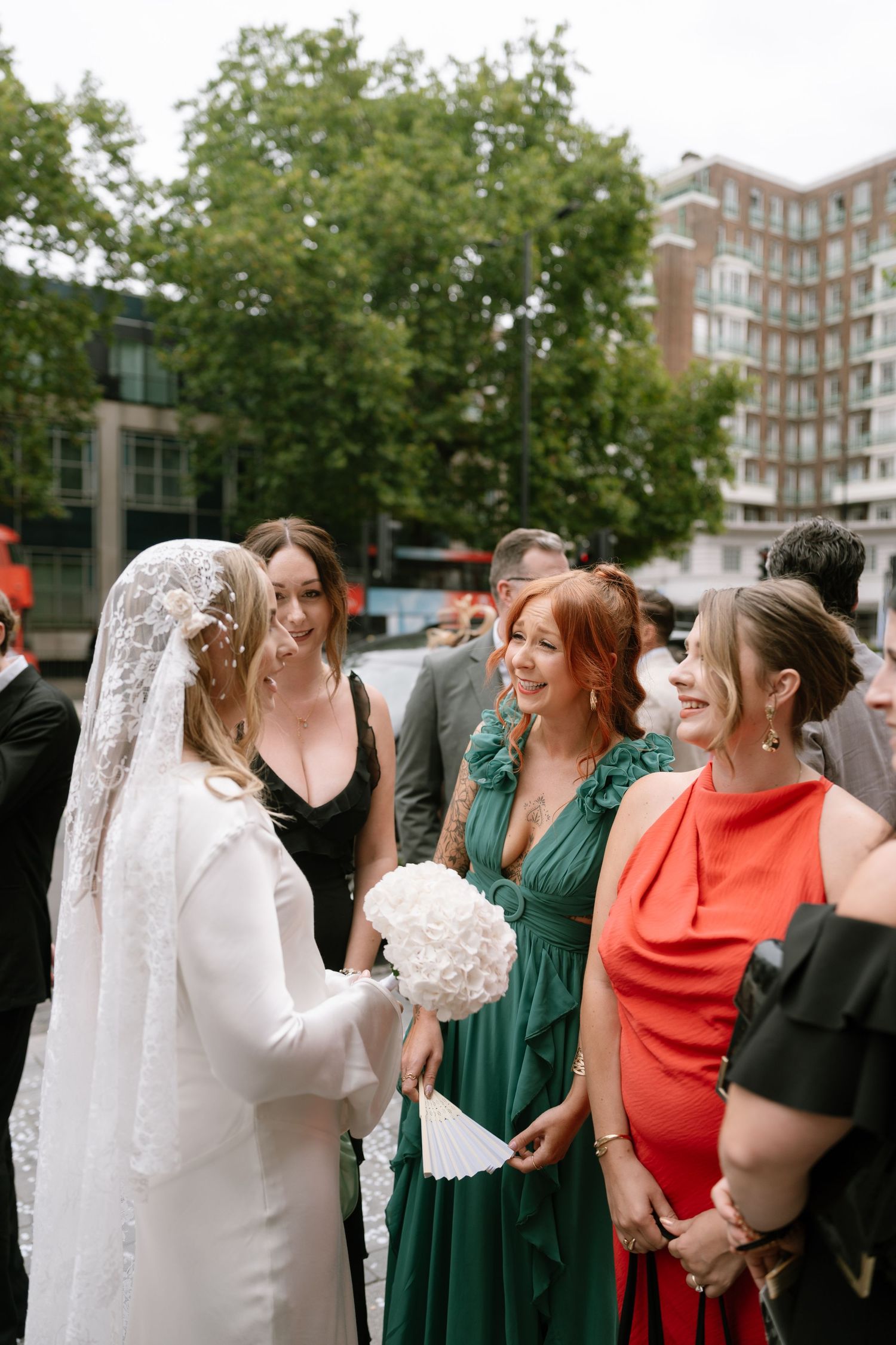 Wedding celebration with guests in colorful dresses gathered outdoors near brick buildings.