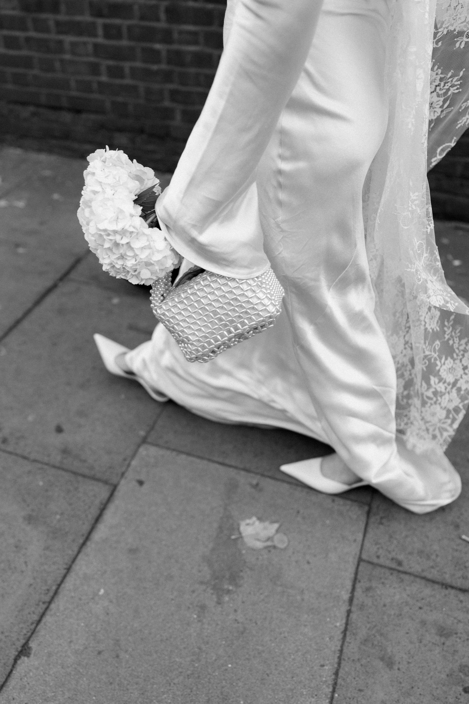 Close-up of wedding dress hem and shoes trailing along a stone pathway.