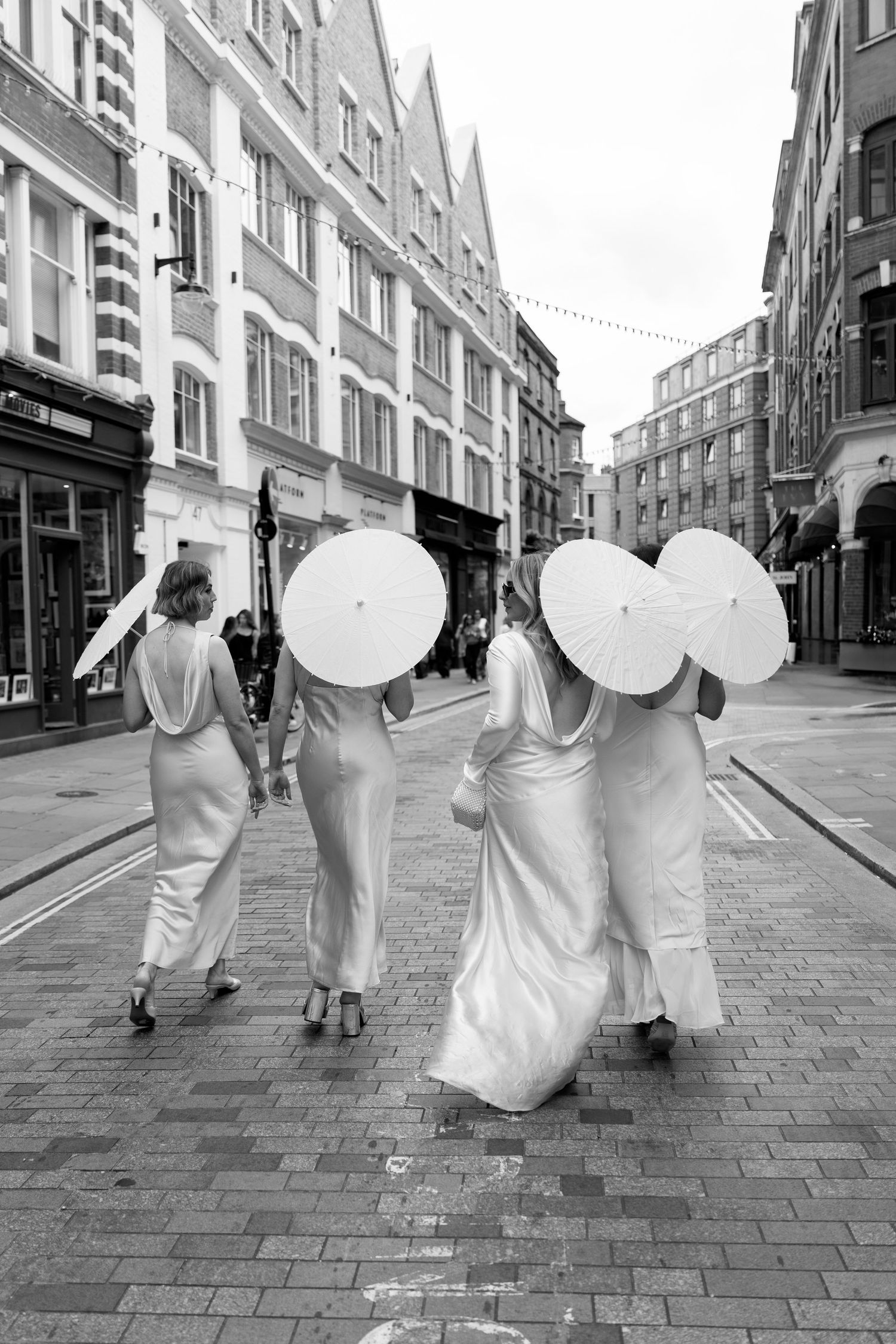 Group walking down cobblestone street in elegant white dresses and formal wear.