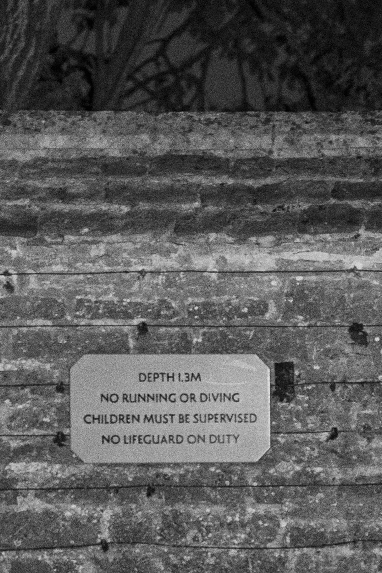 Black and white photo of a pool safety sign reading depth 1.3m, no running or diving.