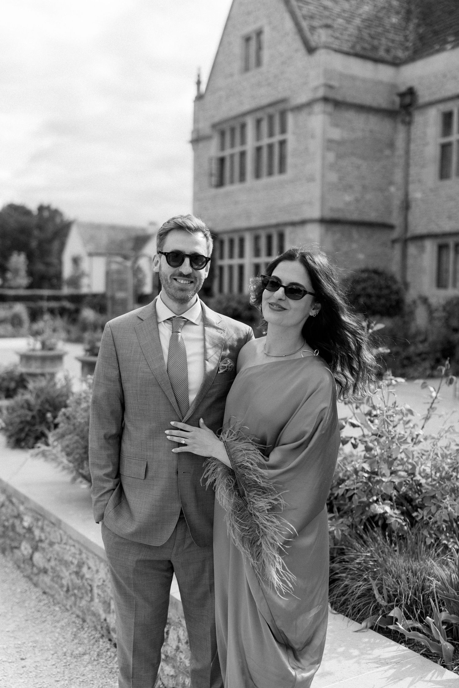 Stylish wedding guests in sunglasses posing in black and white photo outside historic stone manor.