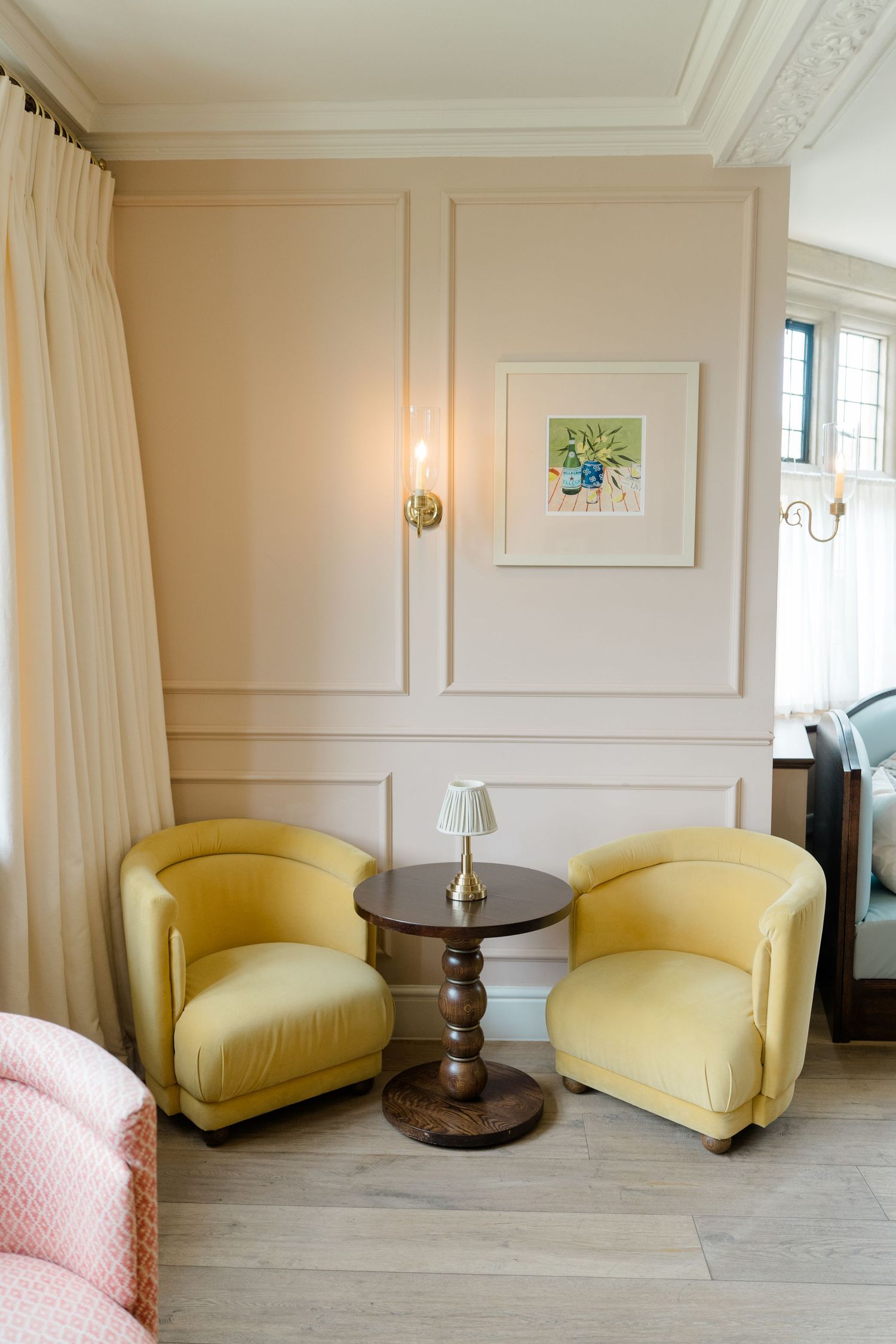 Elegant sitting area with two yellow velvet tub chairs flanking a dark wood pedestal table.