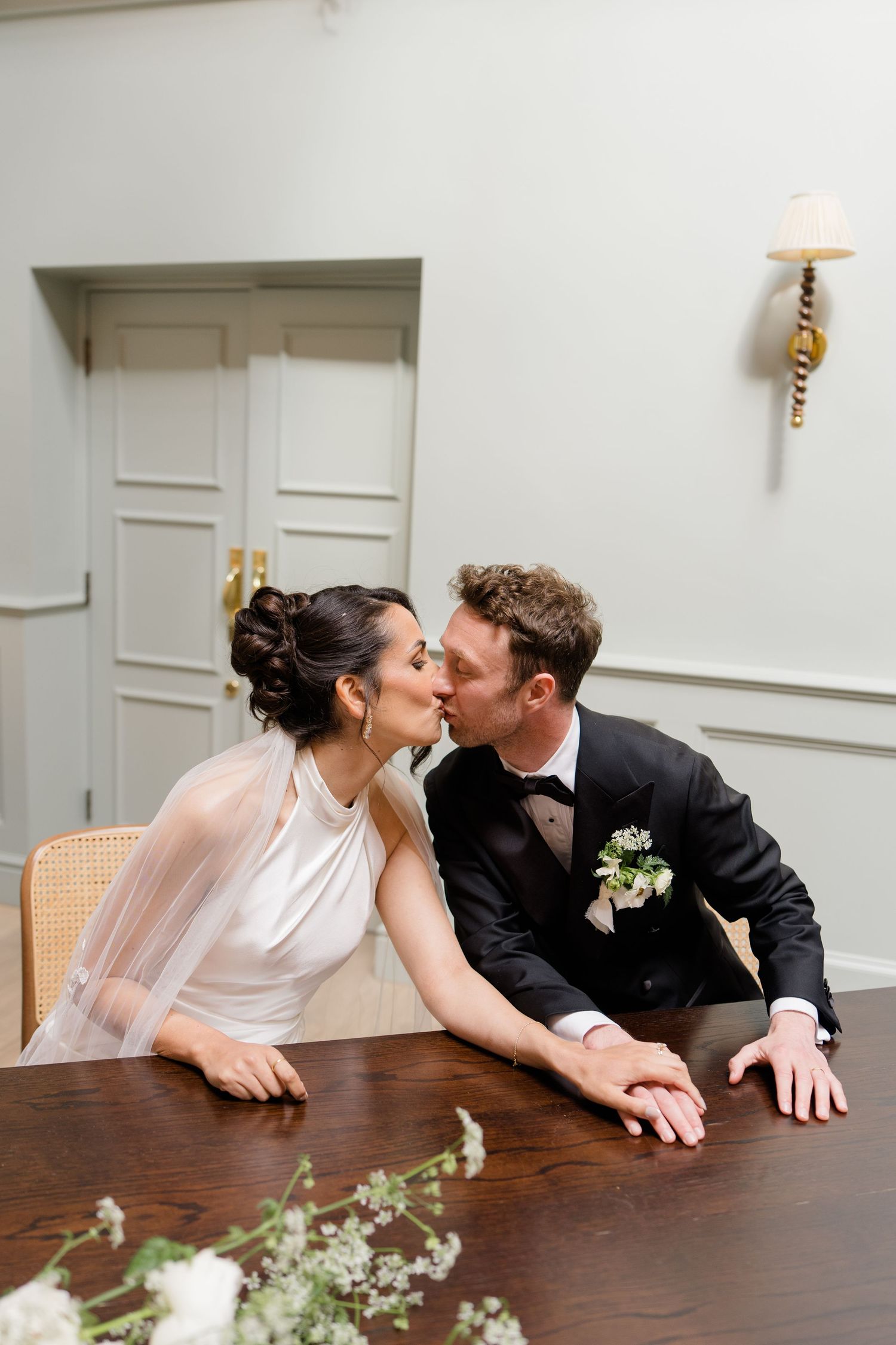 Bride and groom share a romantic kiss at the signing table during their elegant wedding ceremony indoors.