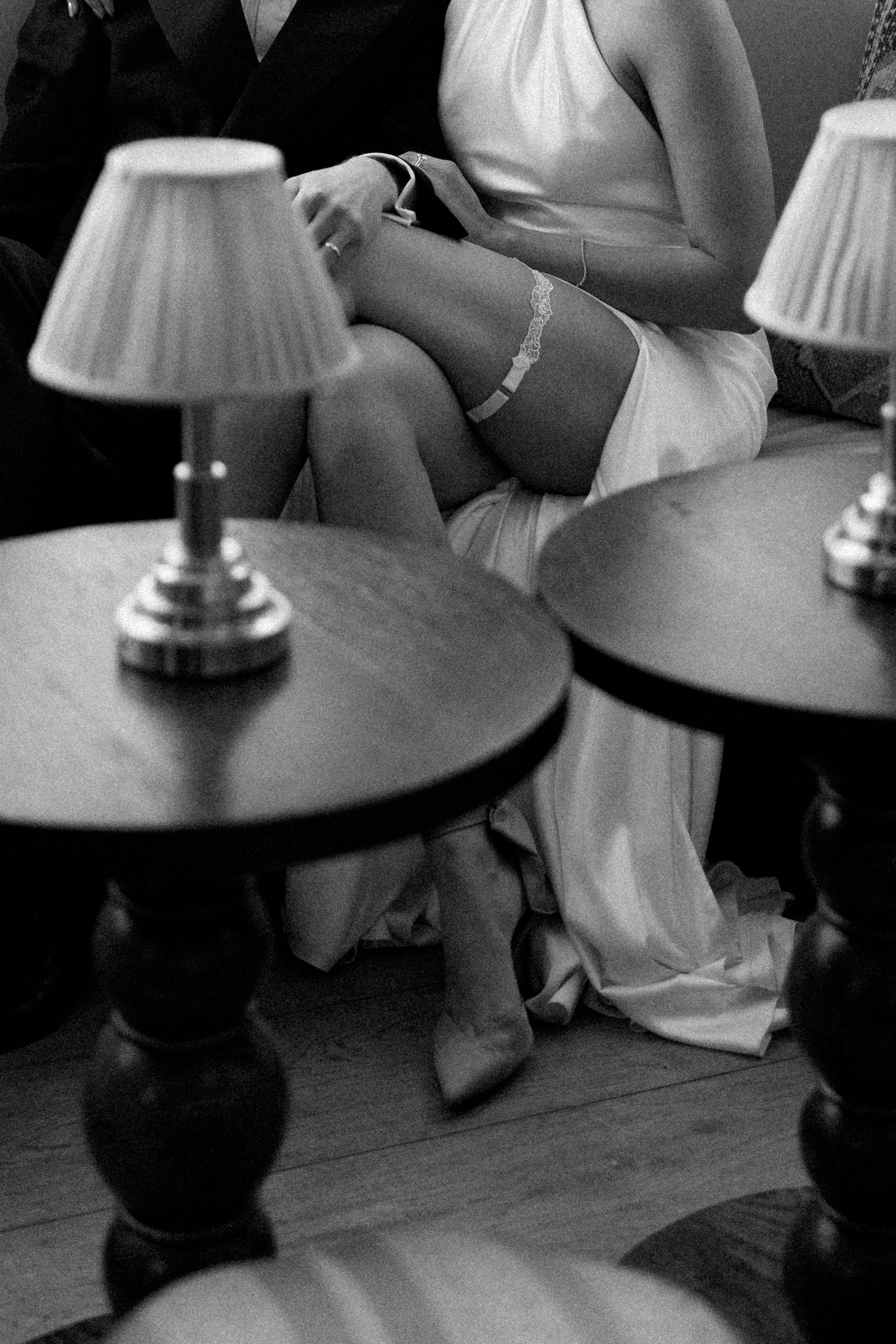 Black and white close-up of bride in white gown with lace garter seated beside groom at wedding.