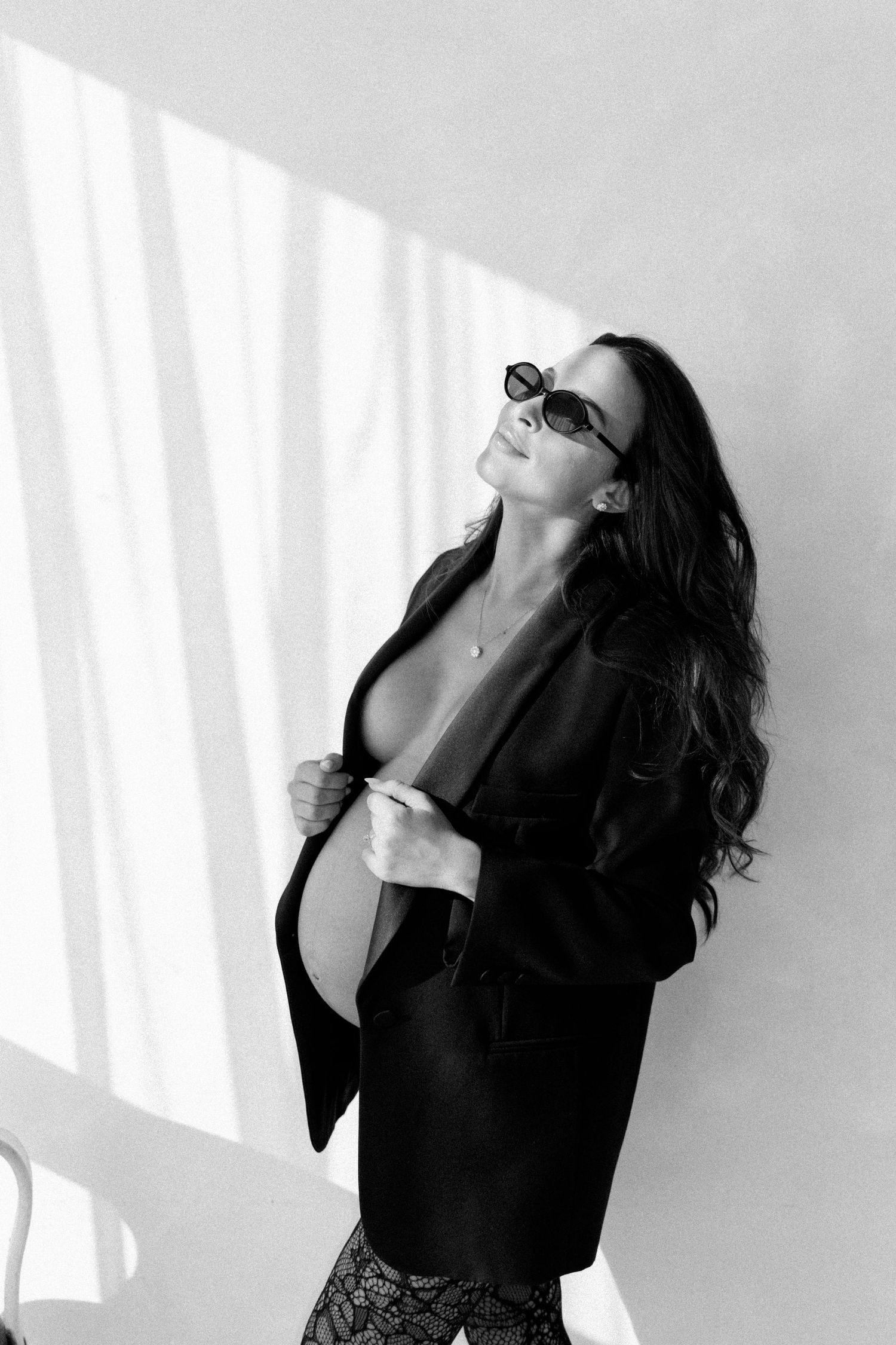 Black and white photo of a woman in sunglasses and blazer posing in dramatic light.