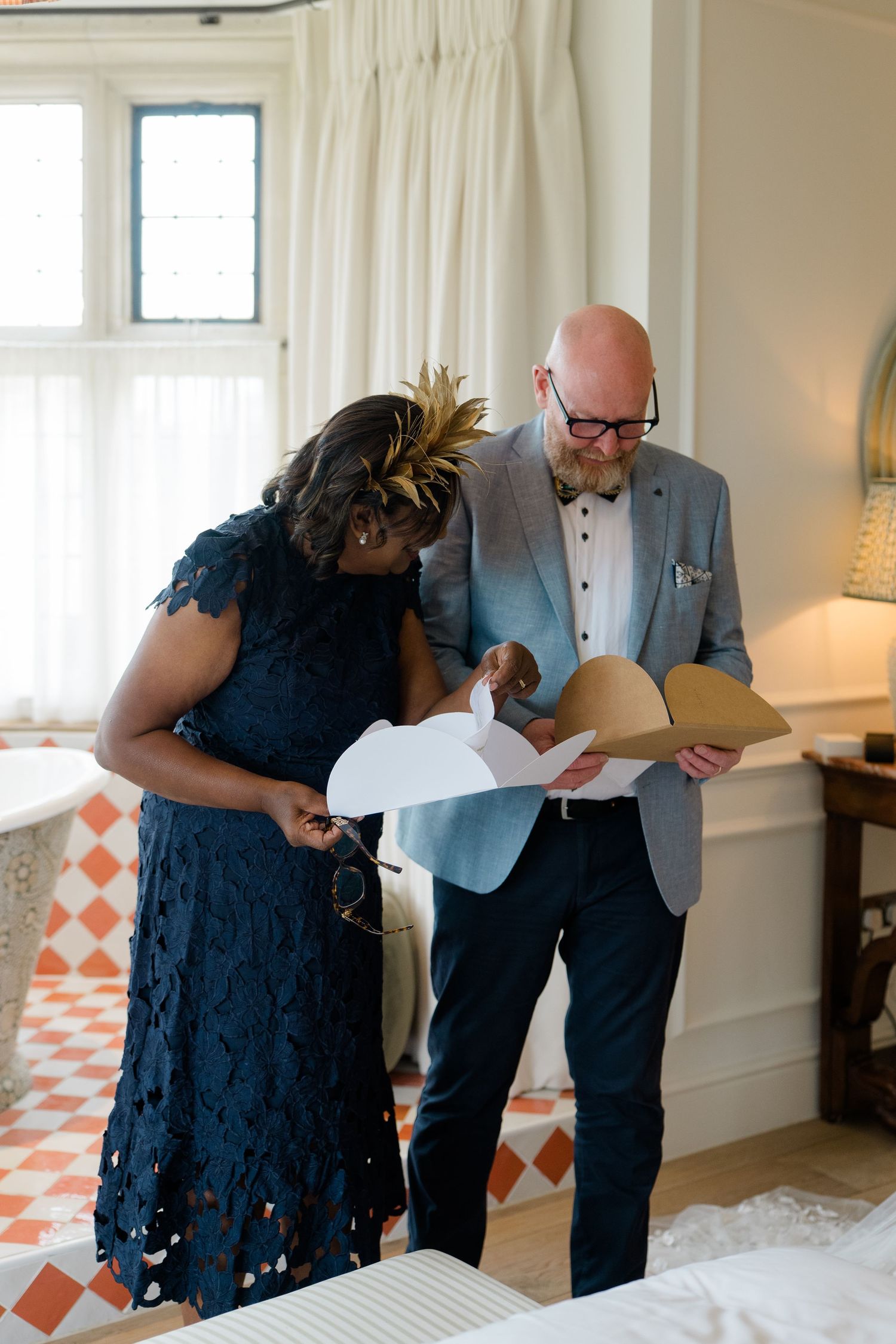 Wedding guests in formal attire review papers together in an elegant tiled room.