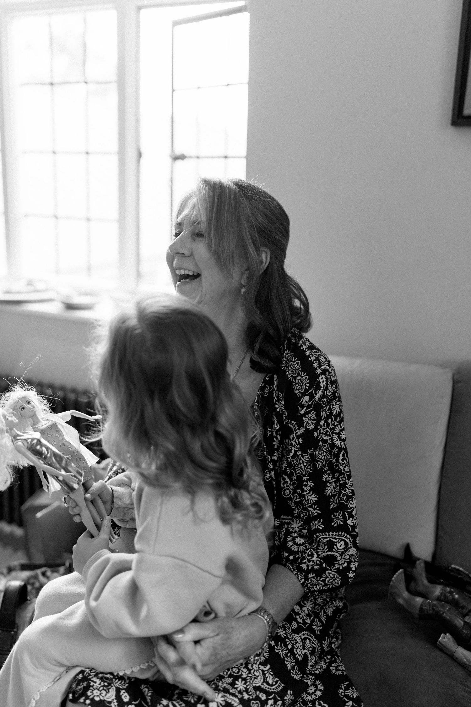 Black and white photo of a laughing woman holding a young child by a bright window.