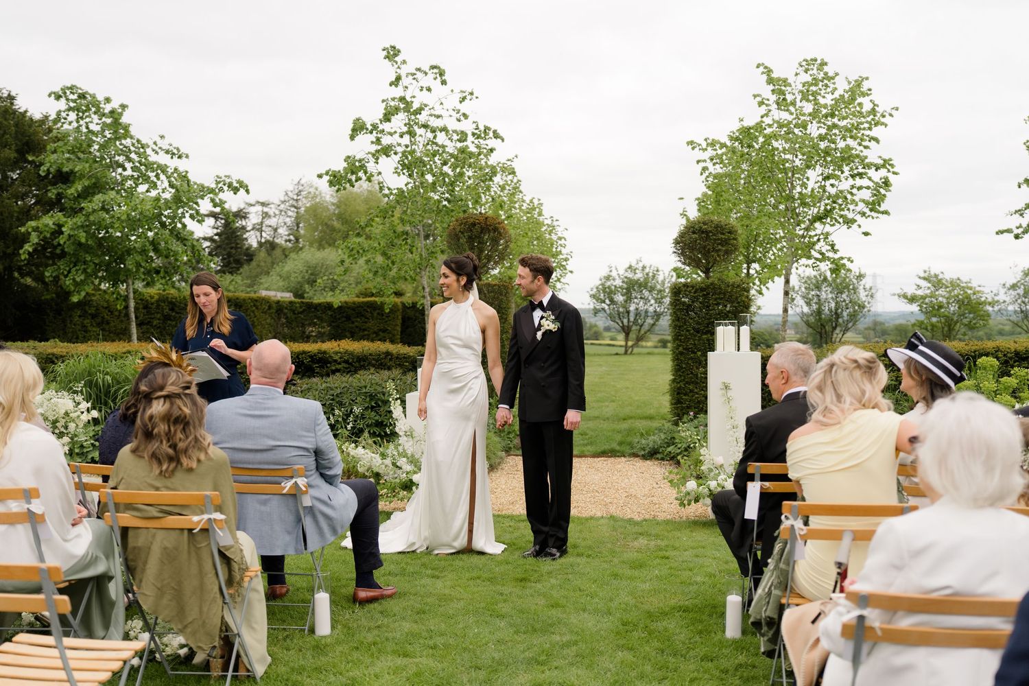 Bride and groom exchange vows at an elegant outdoor garden wedding ceremony with seated guests.