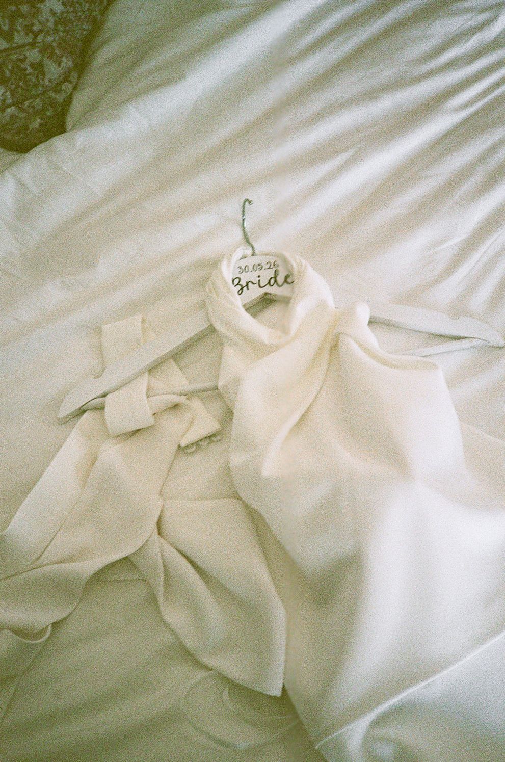 White bridal robe laid on bed with heart-shaped Bride hanger, perfect wedding morning getting ready detail photo.