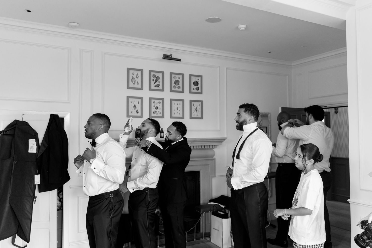 Groomsmen help each other with ties and suits in elegant room before wedding ceremony.