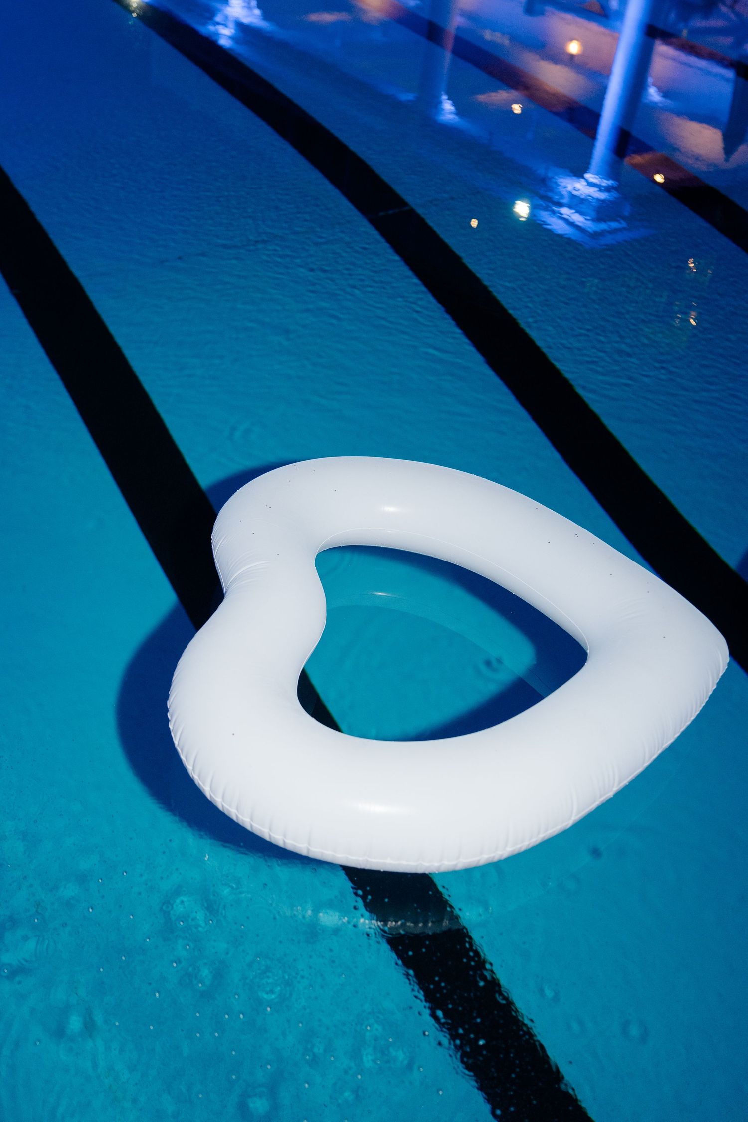 White heart-shaped inflatable pool float floating in a blue swimming pool with lane dividers.