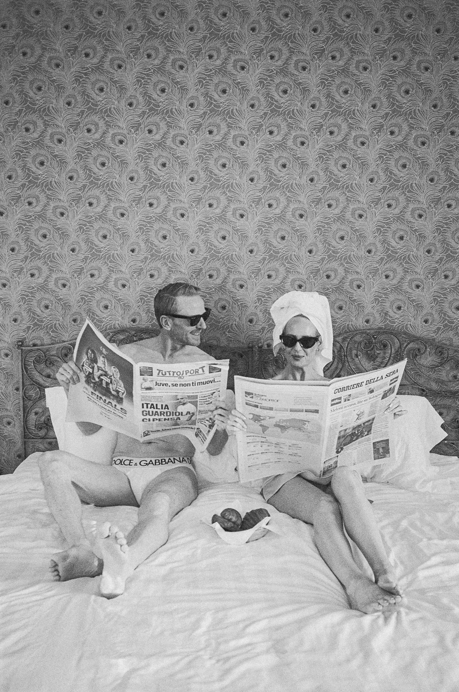 Couple reading Italian newspapers in bed wearing sunglasses, black and white wedding photo.