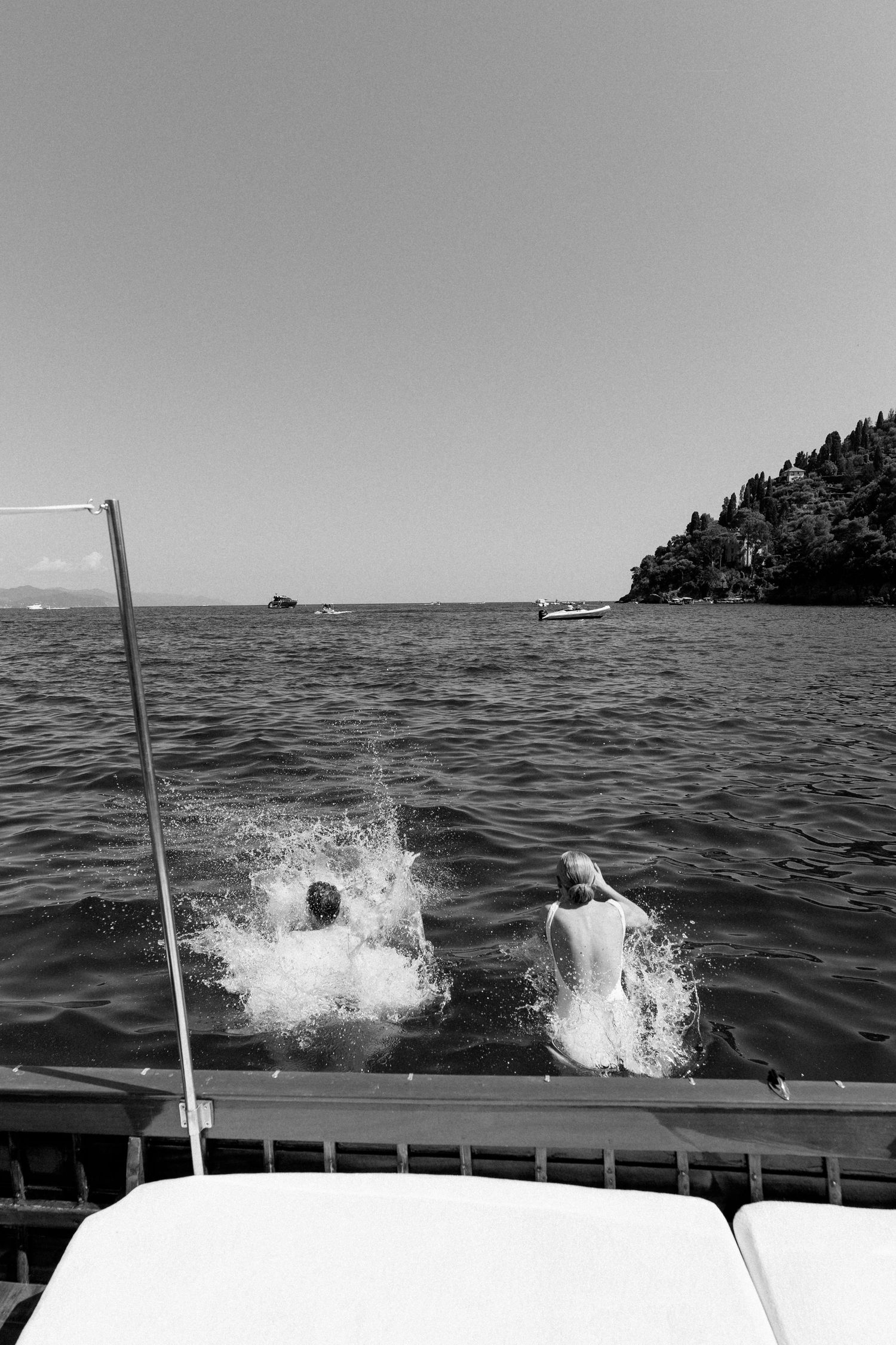 Two people jumping into the sea from a boat in a black and white coastal landscape photo.