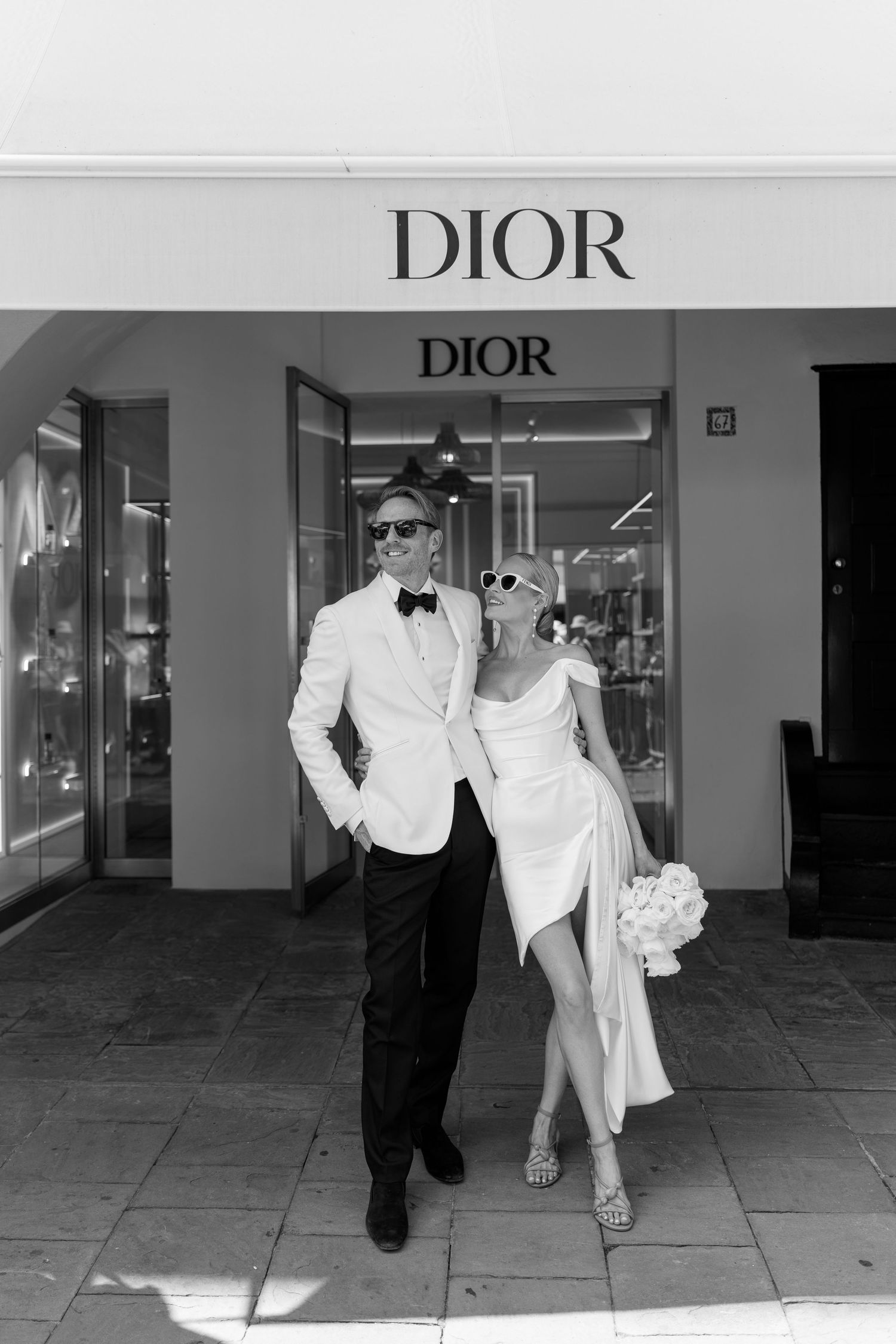 Stylish bride and groom posing in black and white outside a luxury Dior boutique on their wedding day.