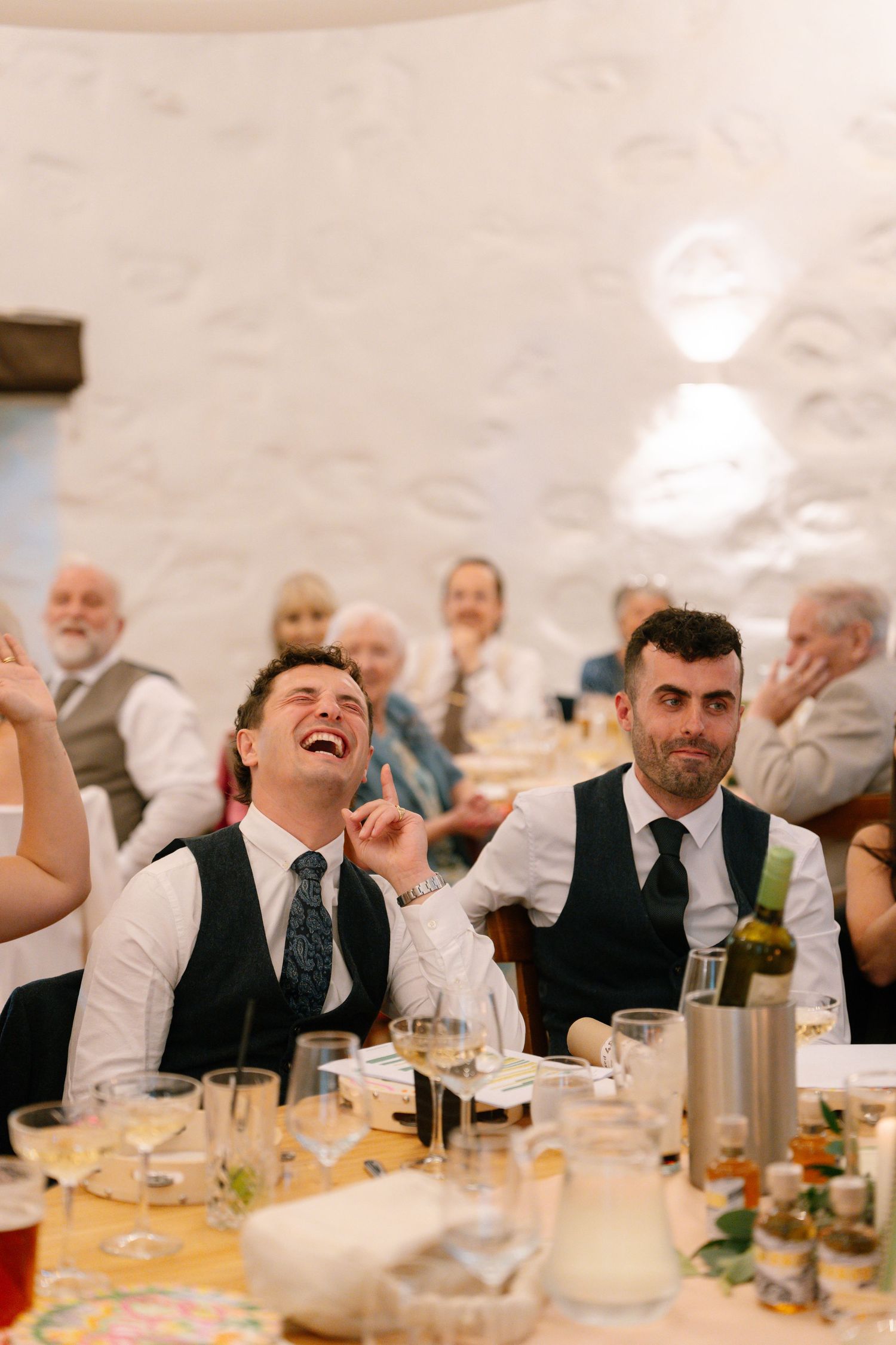 Wedding reception guests laugh and celebrate at tables during dinner.