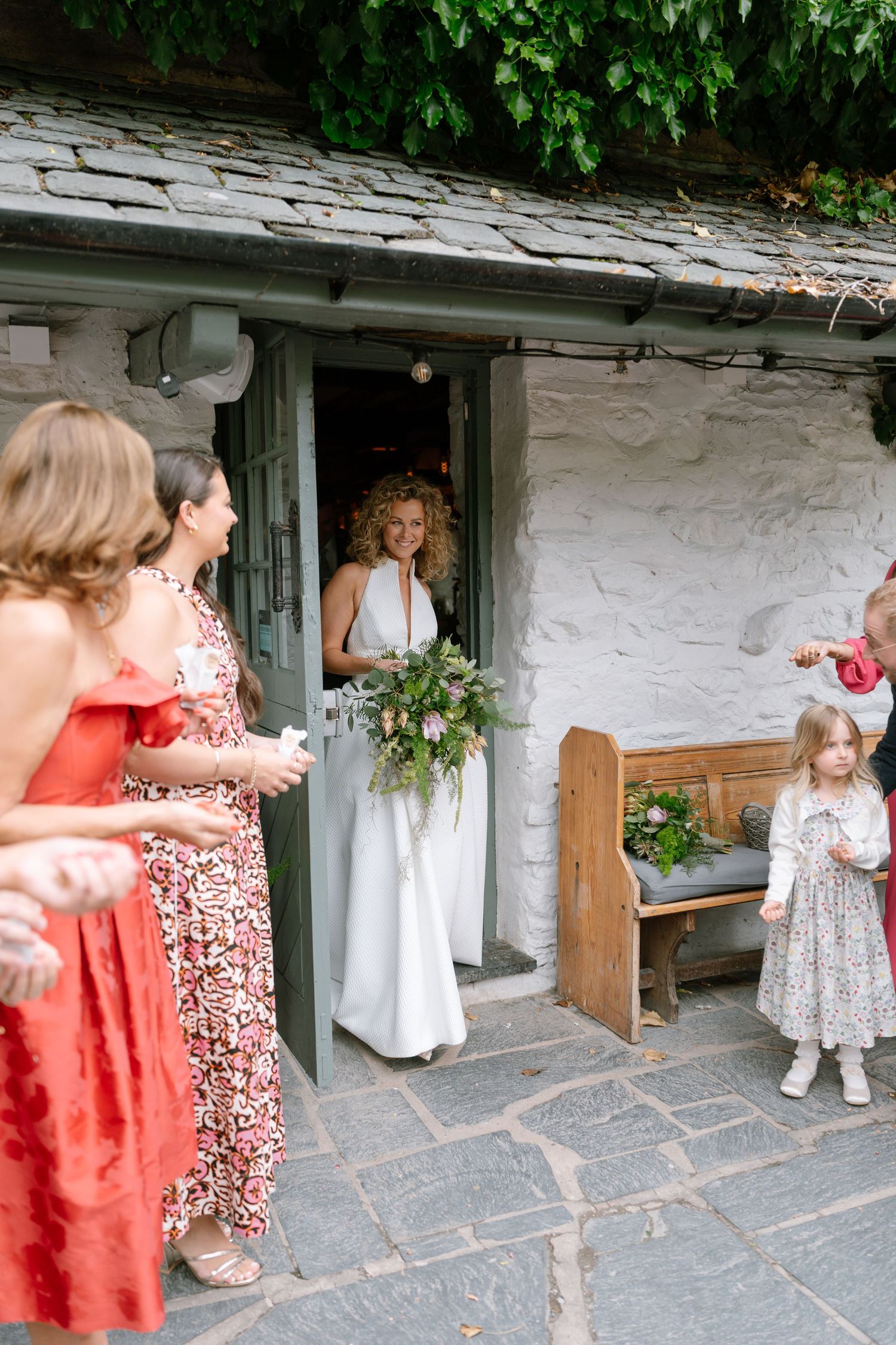 Wedding party preparations outside a rustic stone building with floral decorations.