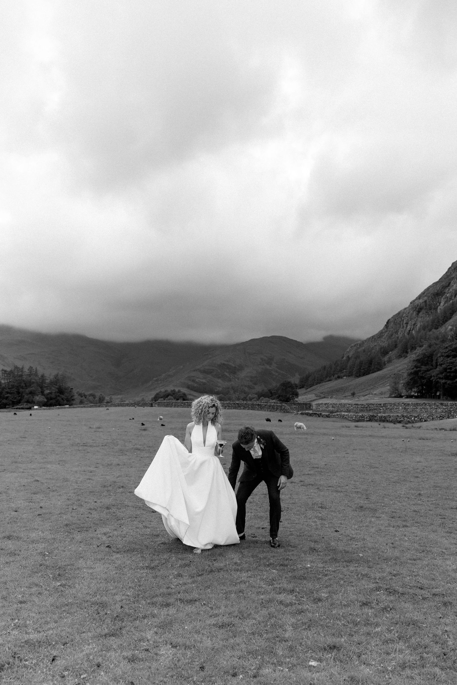 Couple walks together across scenic field with mountains in background in black and white.