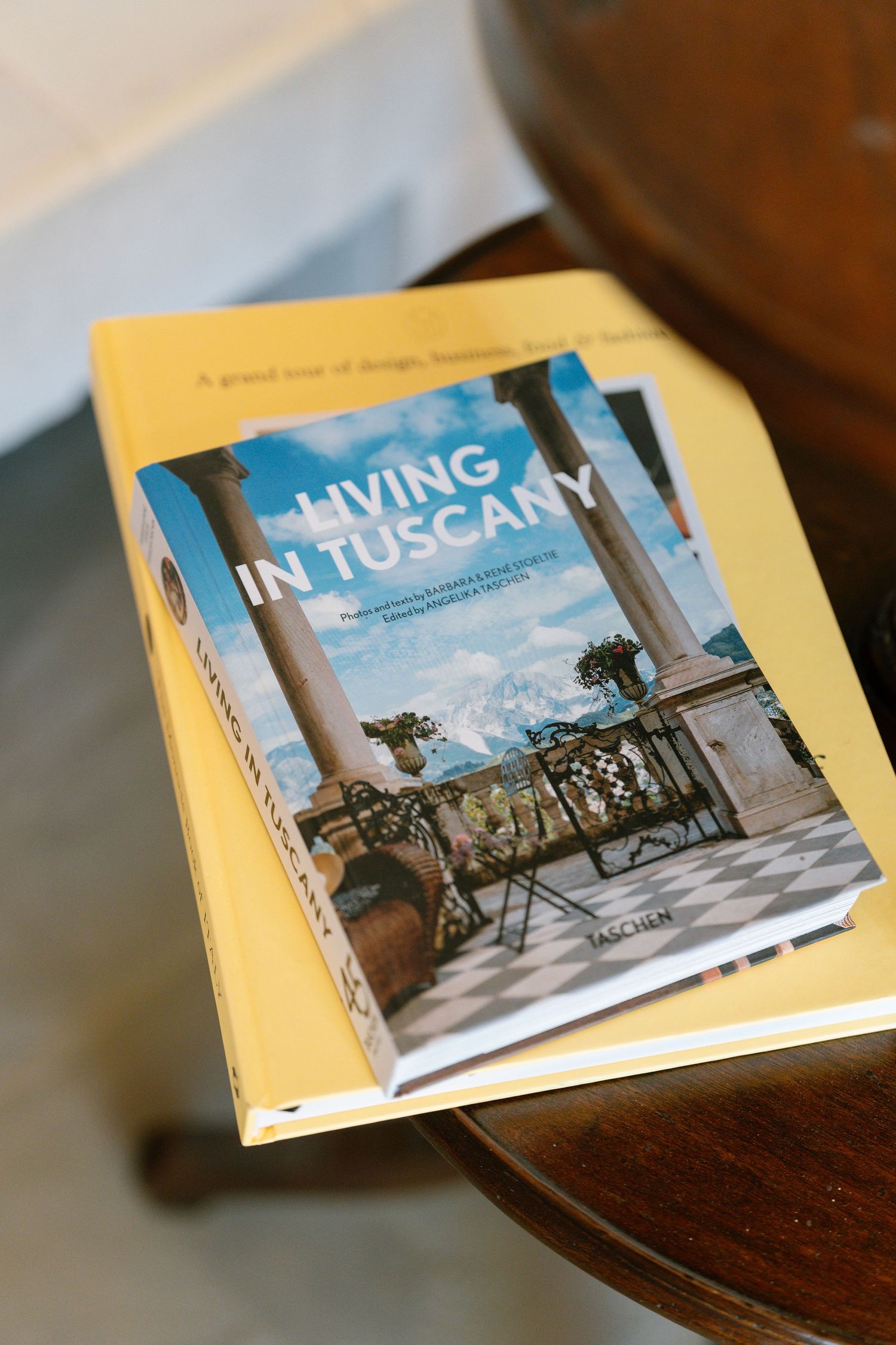 Multiple views of a hardcover photography book titled 'Living in Tuscany' displayed on a wooden surface.