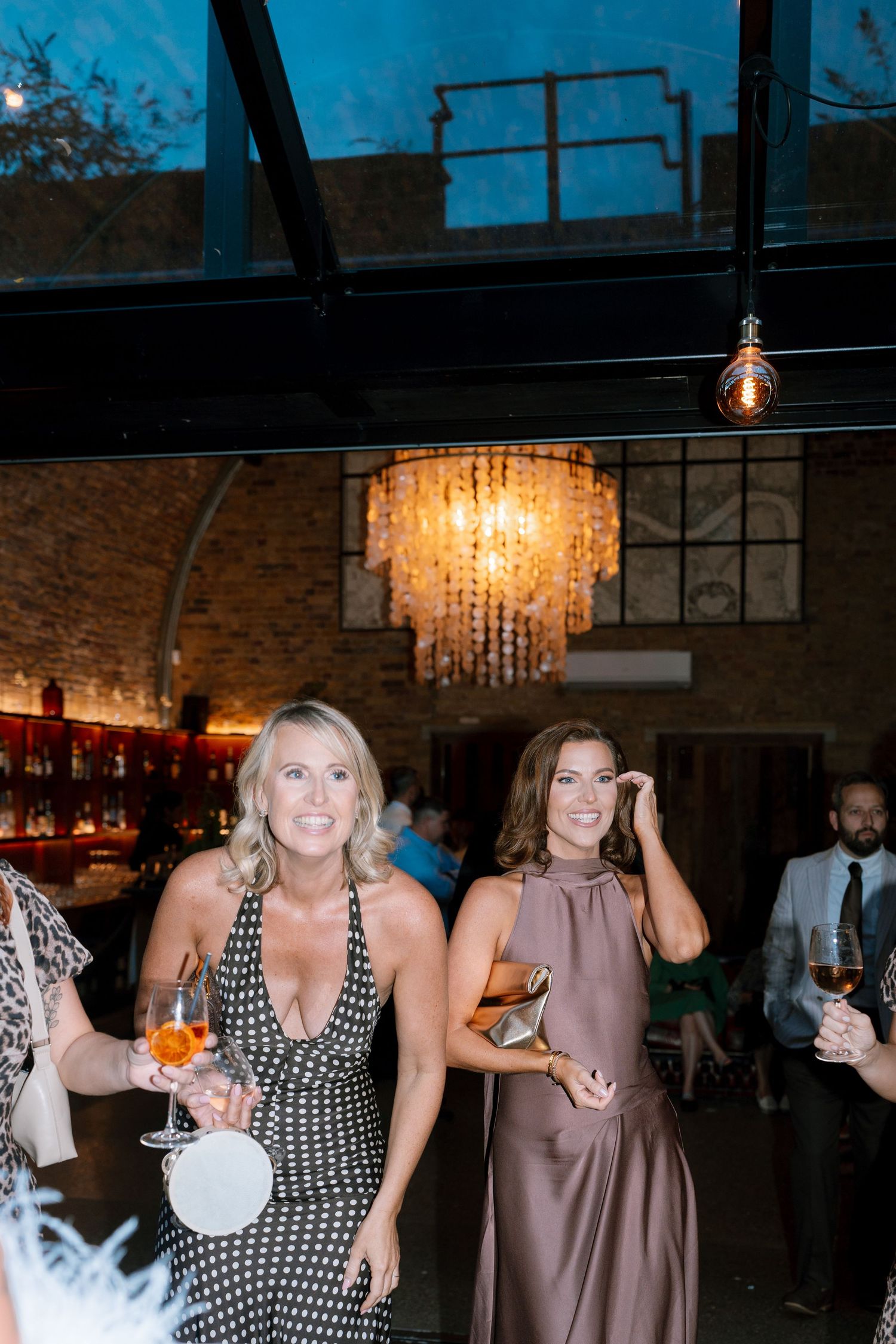 Wedding reception venue with crystal chandeliers and guests enjoying drinks at the bar.
