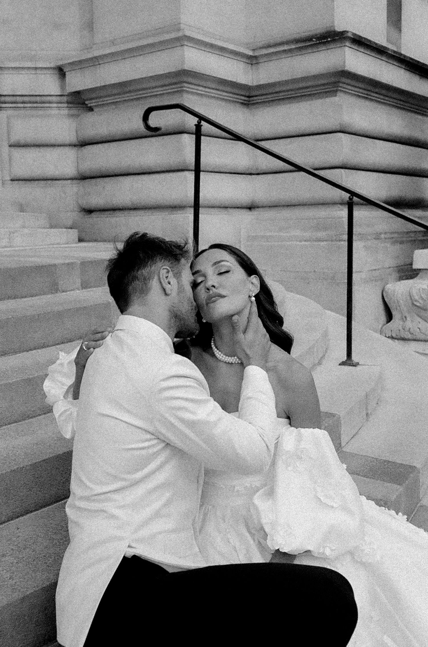 A romantic black and white wedding photo of a couple sharing an intimate moment on stone steps.